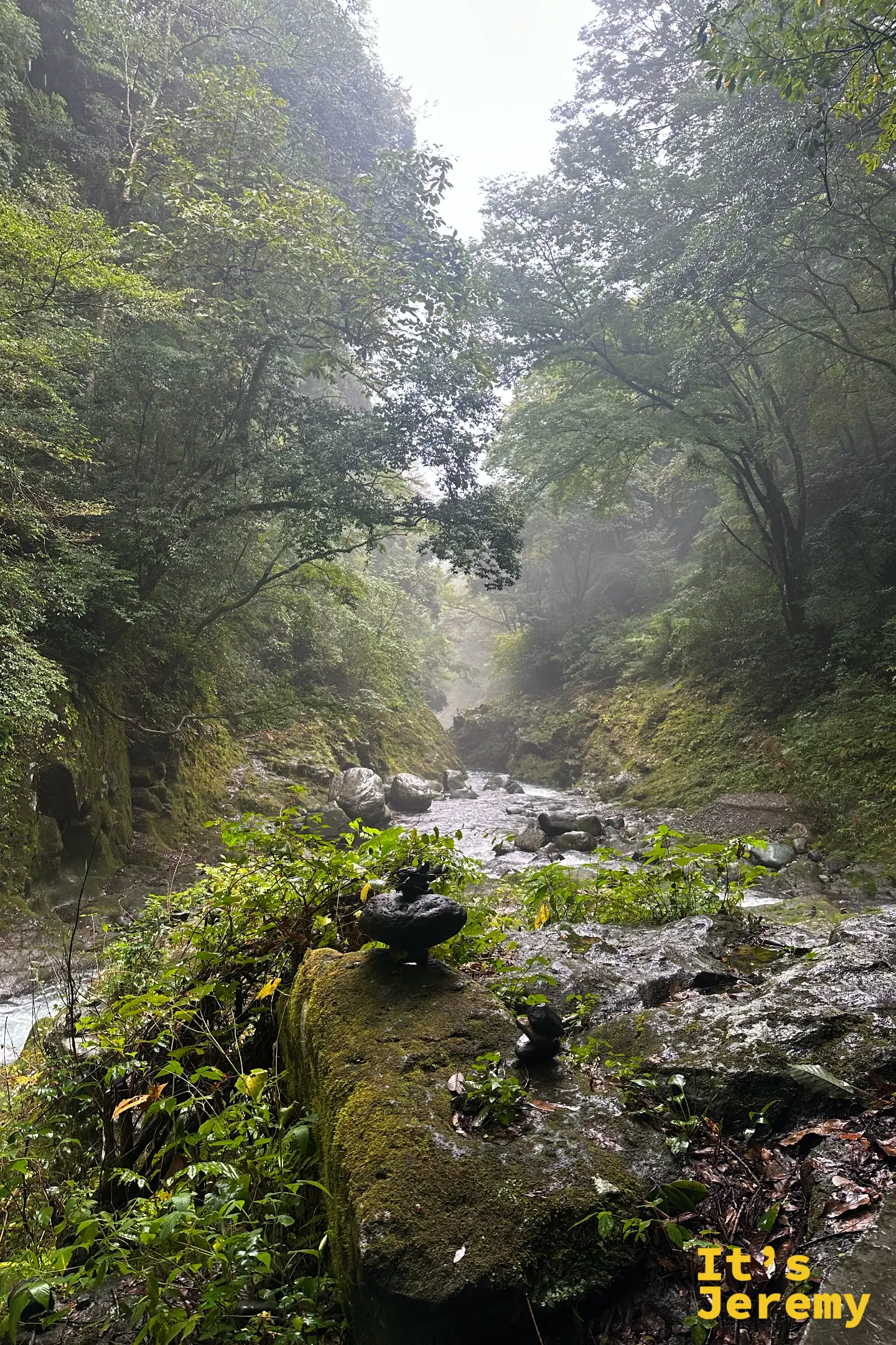 通往天安河原的岩戸川溪谷，雨霧繚繞，溪流兩側的石頭上堆著大大小小的祈願石塔