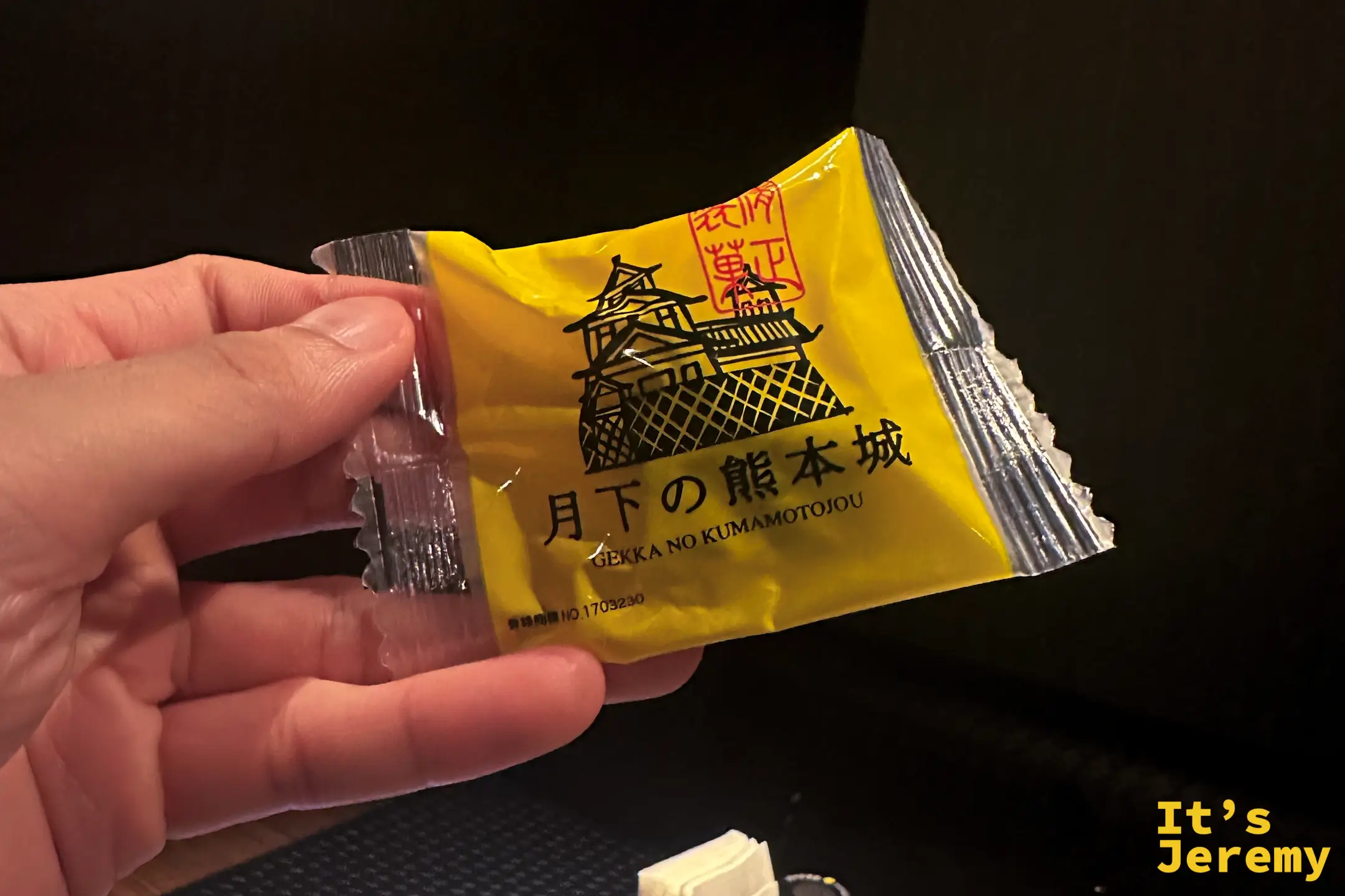 手拿黃色包裝的和菓子「月下の熊本城」