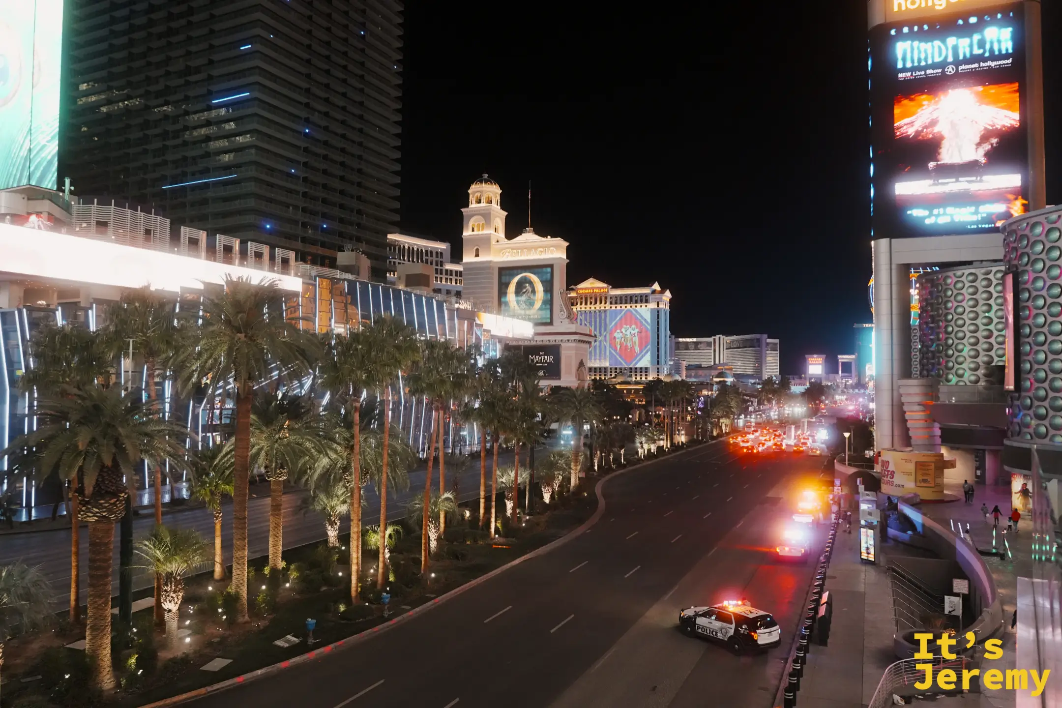 從天橋俯瞰入夜的大道，Bellagio 與 Caesars Palace 的燈火沿著棕櫚樹延伸