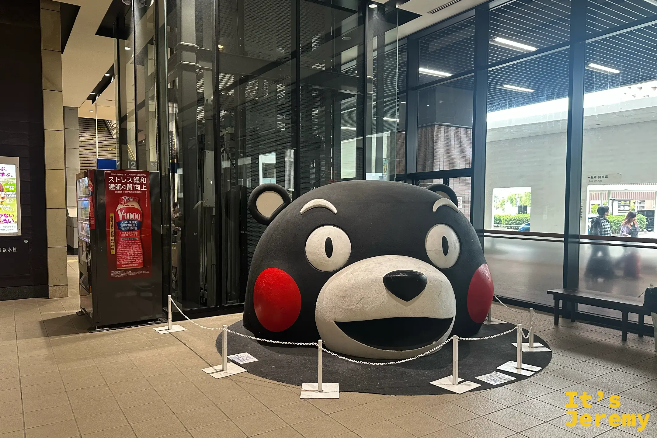 熊本站大廳裡熊本熊（くまモン）的巨大頭部塑像，黑色身體、紅臉頰，前方用鏈條圍出合影區