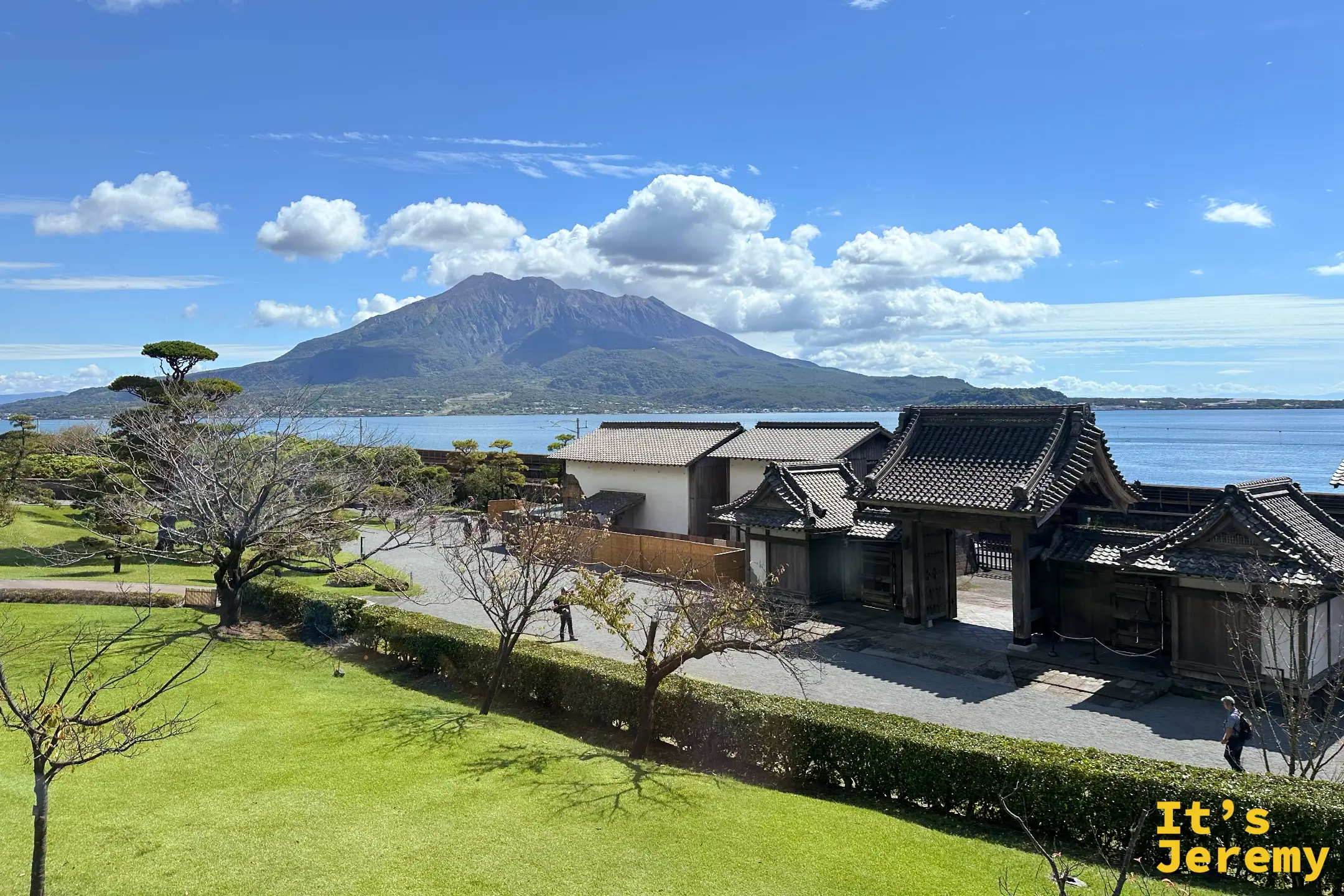 從餐廳望向仙巌園庭園，翠綠草坪、傳統瓦頂建物，錦江灣對岸是雲頂的櫻島火山