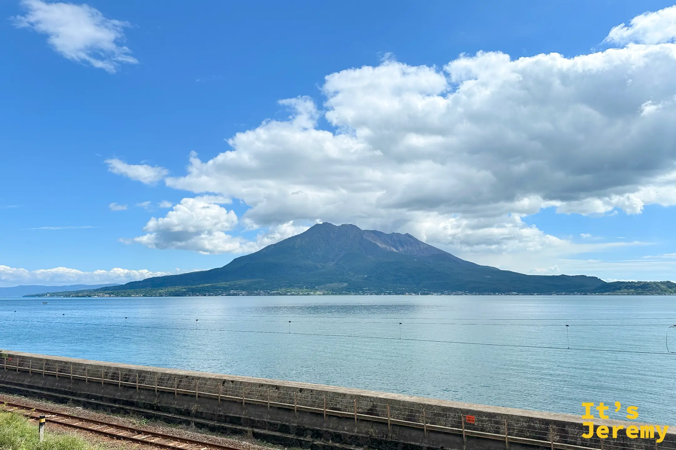 錦江灣對岸的櫻島全景，藍天下三峰並列，海面平靜