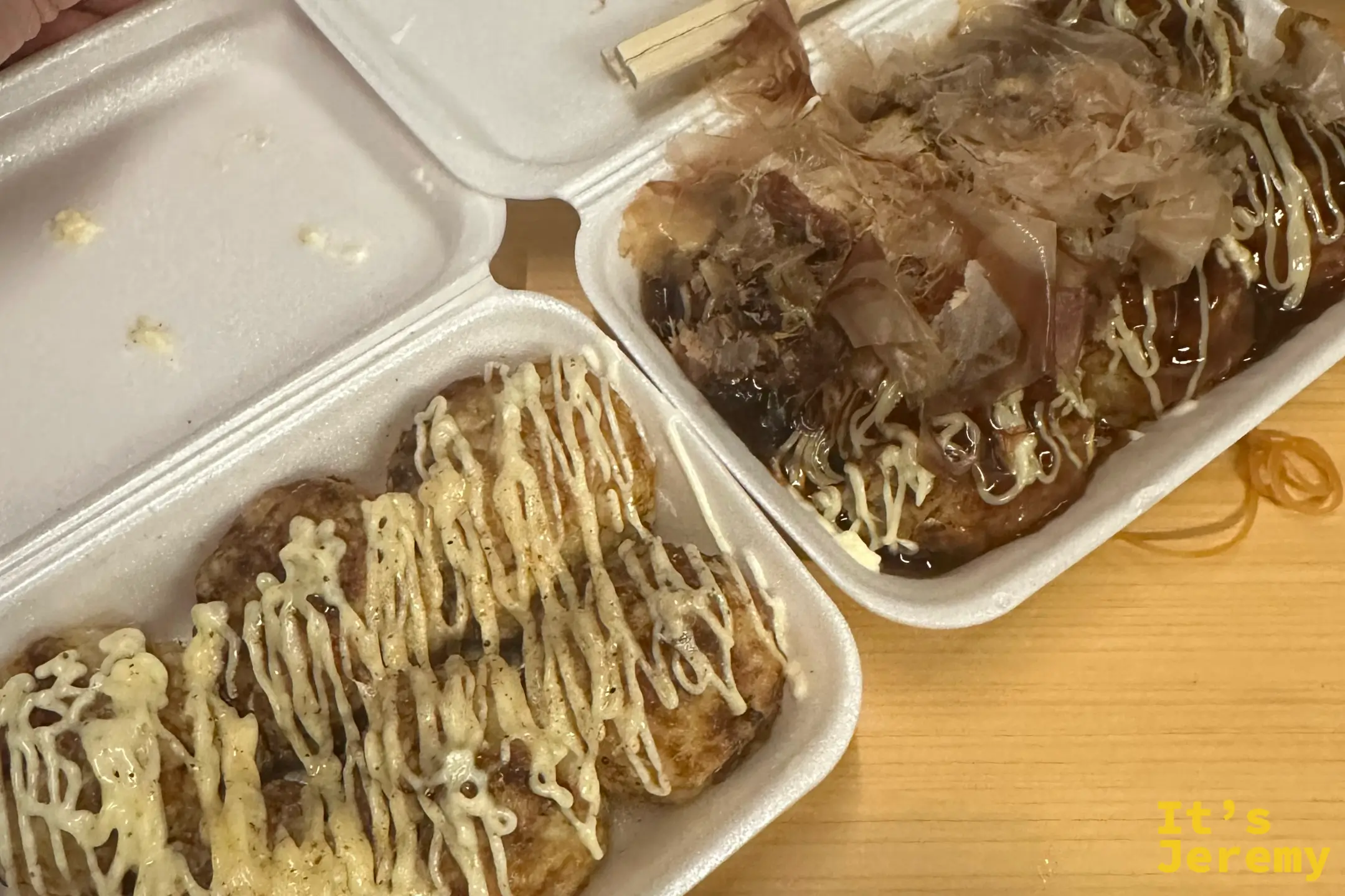 打開的保麗龍盒裡裝著兩盒章魚燒，左邊是撒上胡椒與美乃滋的鹽味，右邊鋪滿柴魚片、淋上濃醬與美乃滋的醬汁口味