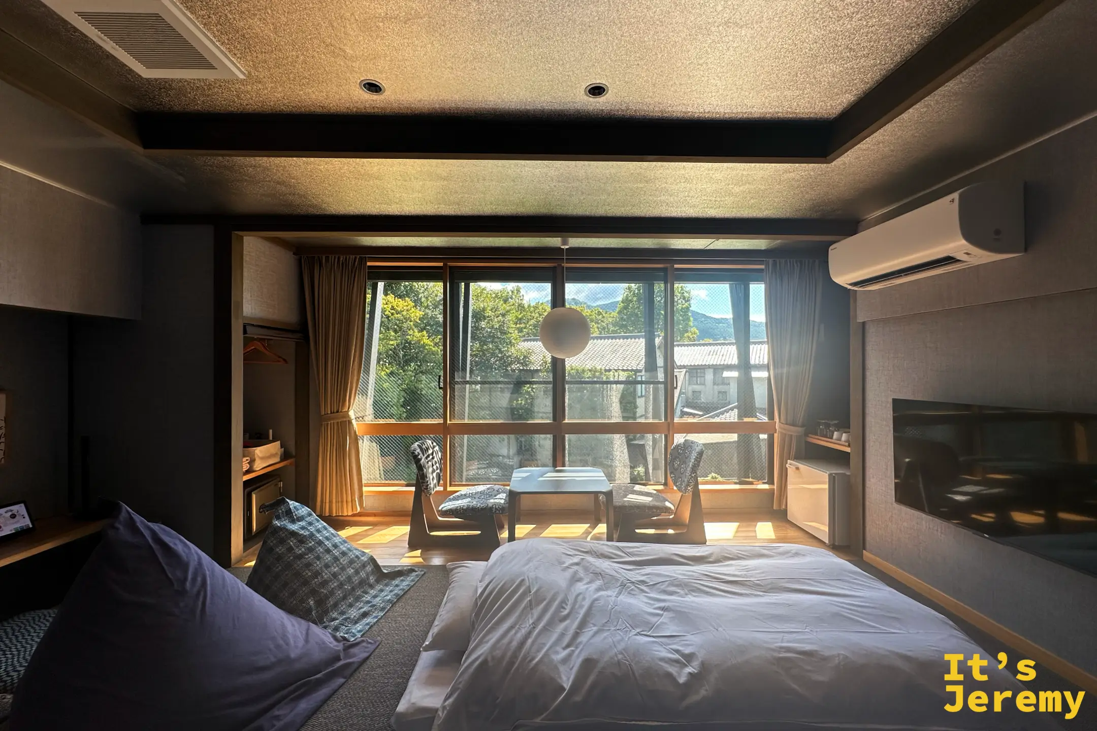 榎屋旅館雙人房，一張大床搭配窗邊矮椅與茶几，電視與冷氣，陽光灑進