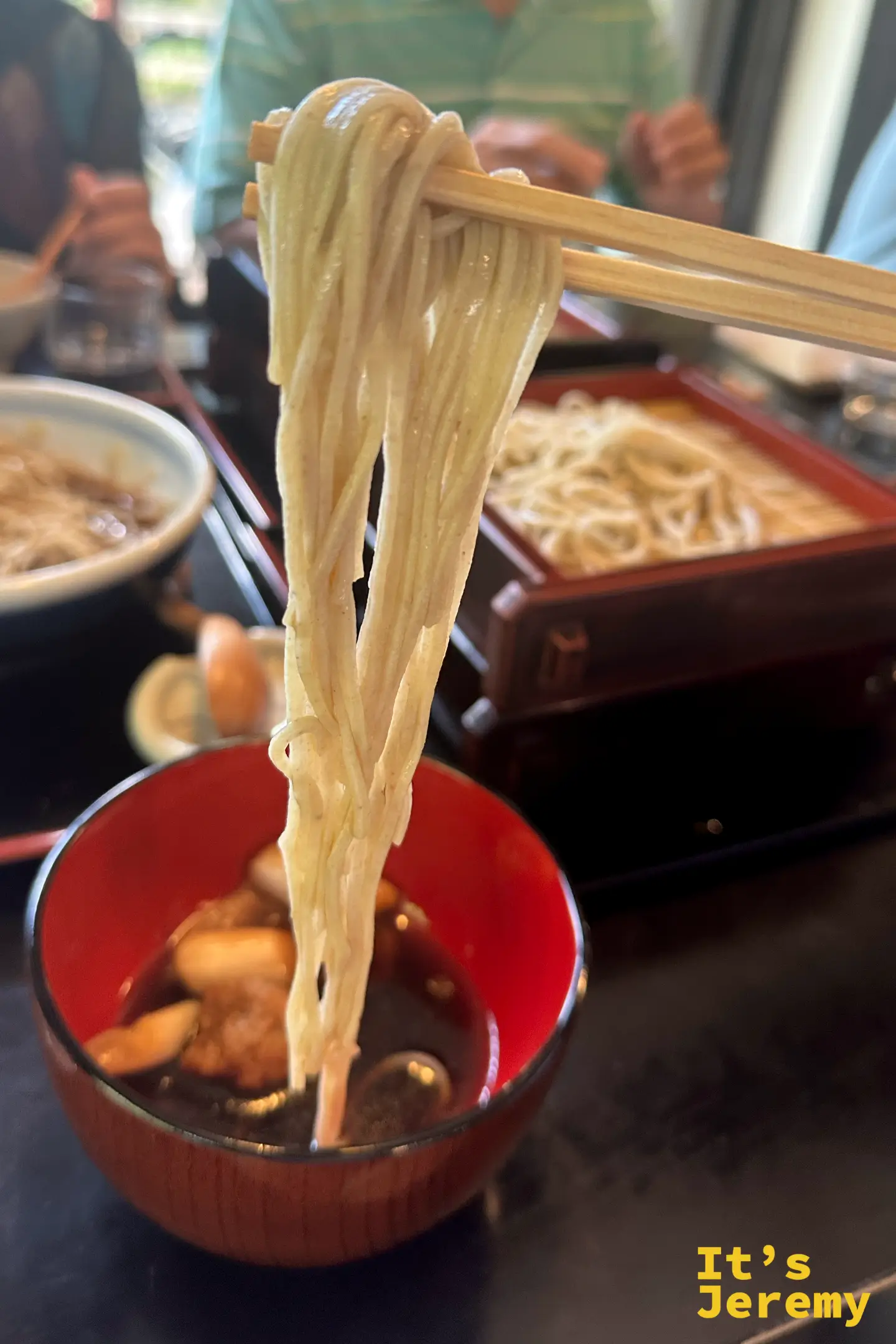 筷子夾起一大束泉的手打蕎麥麵特寫，麵條粗、呈粉褐色、表面霧面