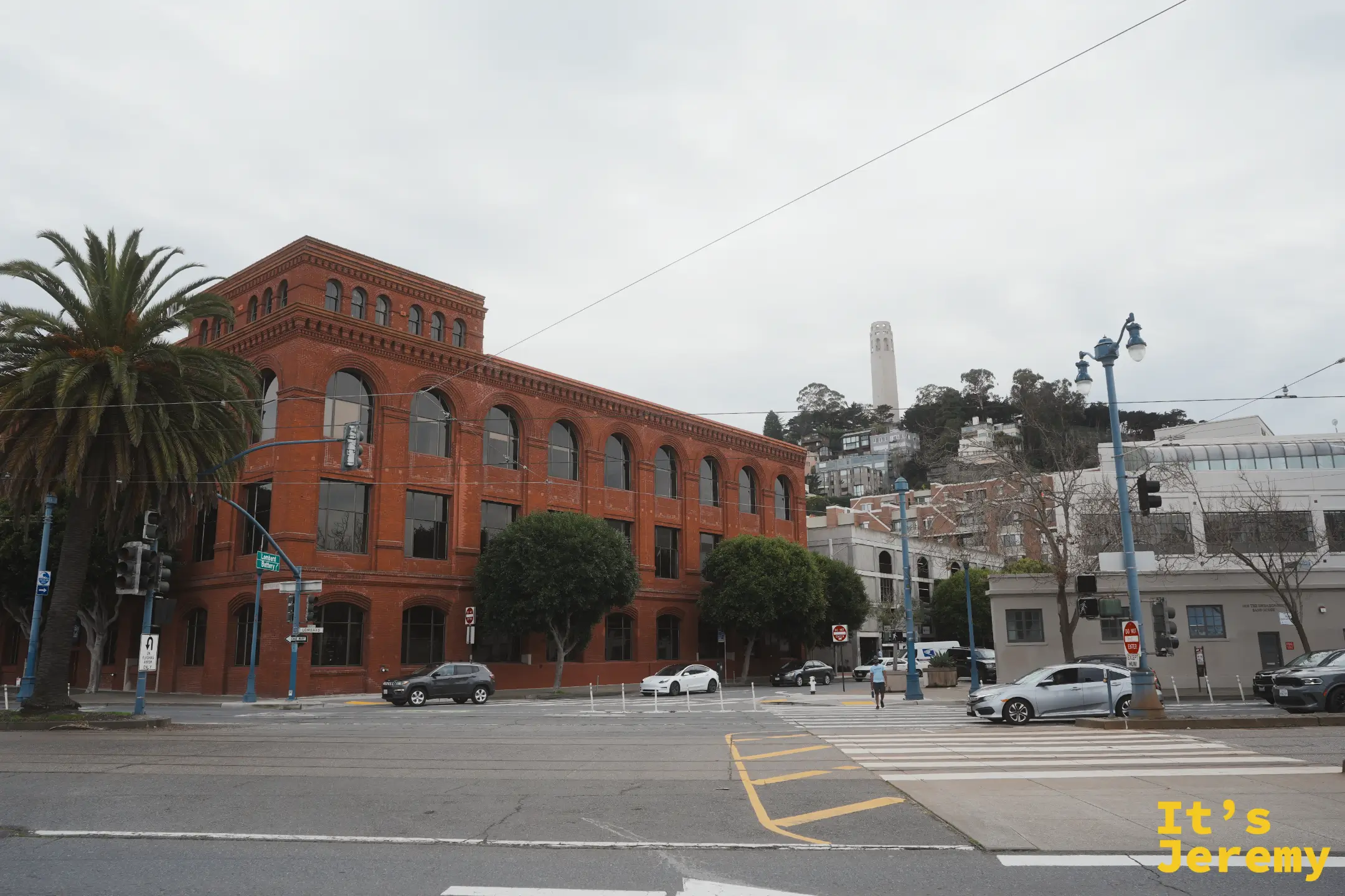 街角一棟紅磚老建築，後方電報山上立著白色的科伊特塔 Coit Tower