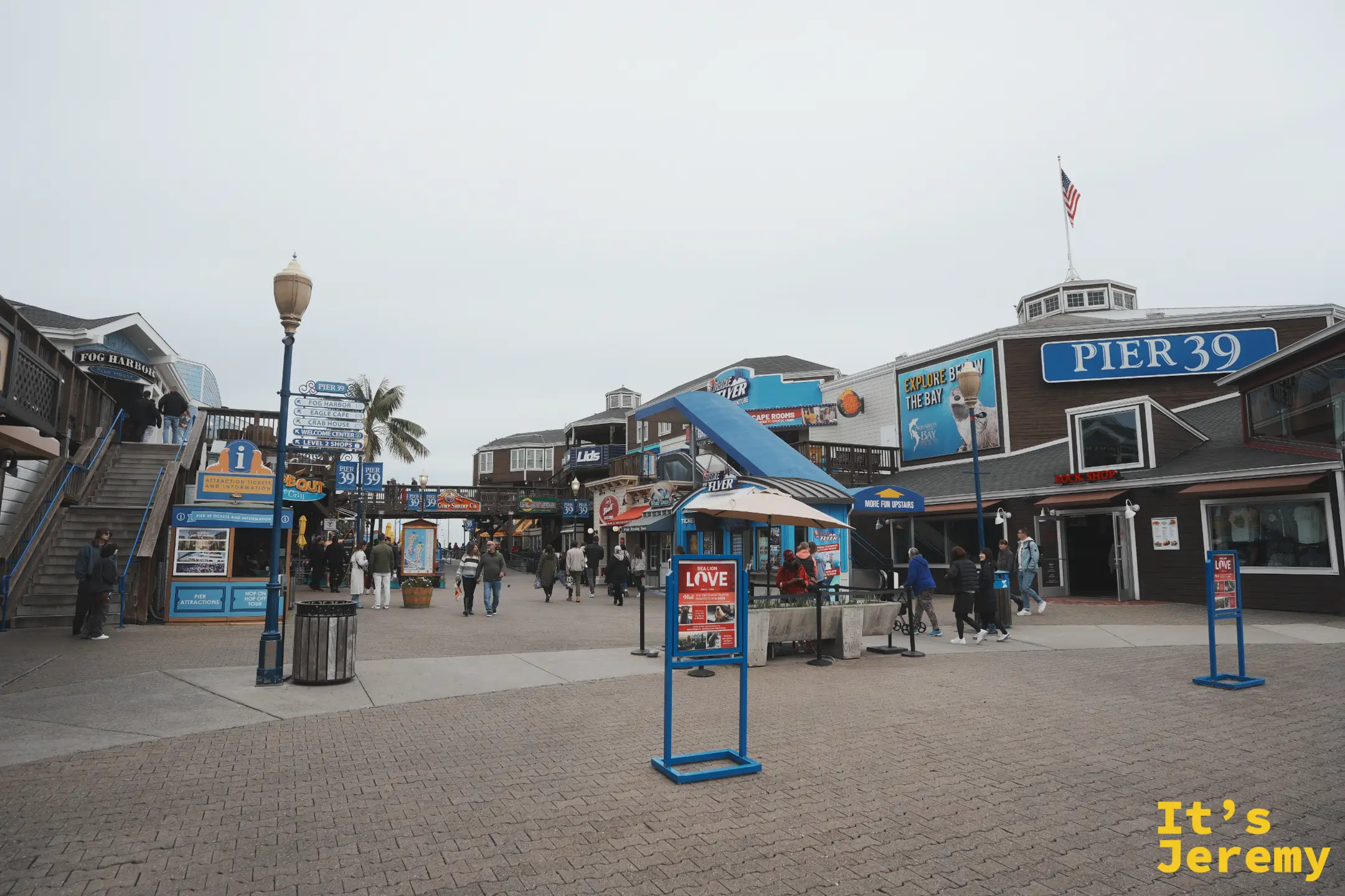 深藍底白字的 PIER 39 大型招牌立在木造建築上，屋頂飄著美國國旗