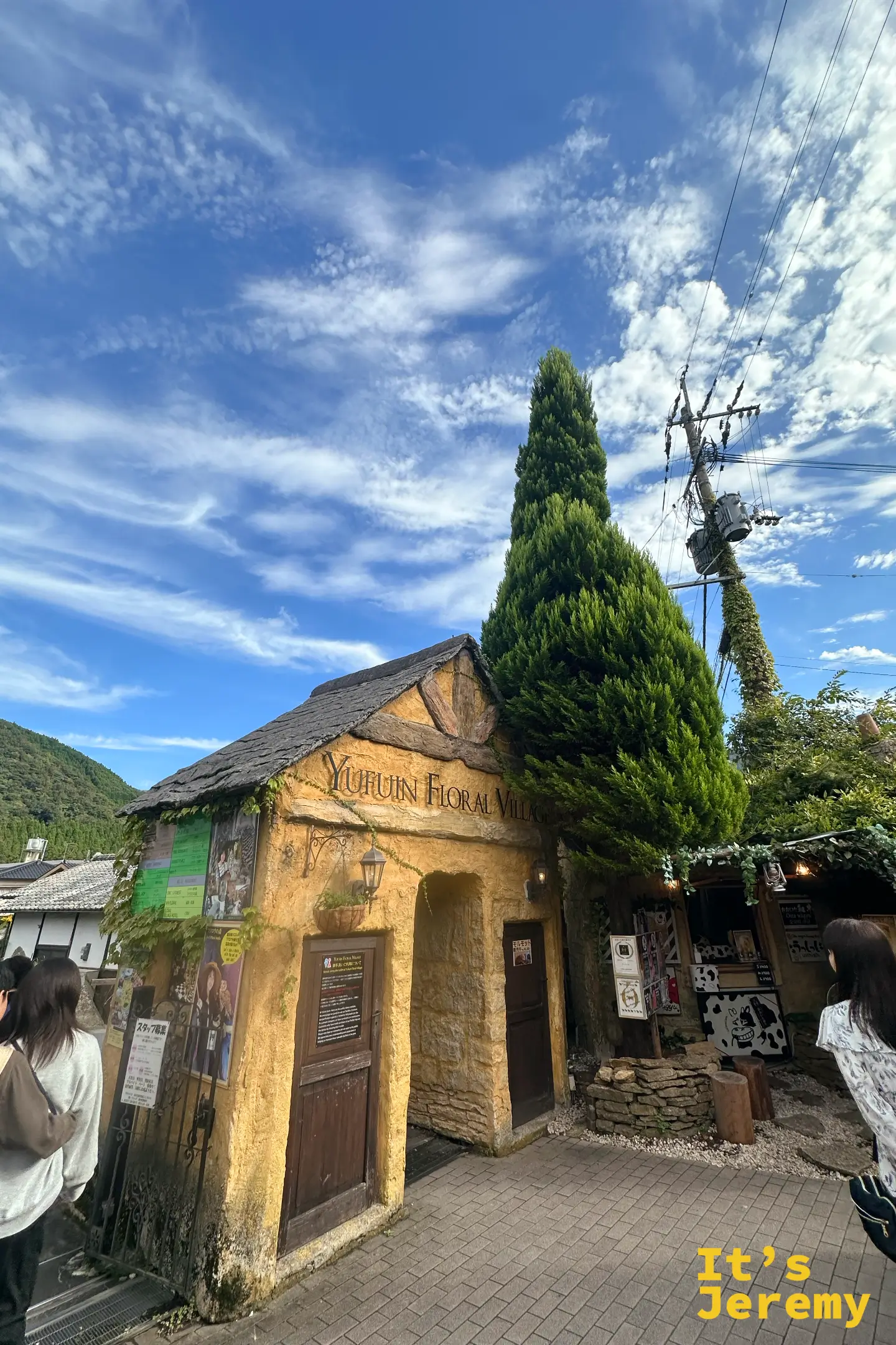 Yufuin Floral Village 入口的黃土色童話小屋，石板屋頂與尖塔般的柏樹