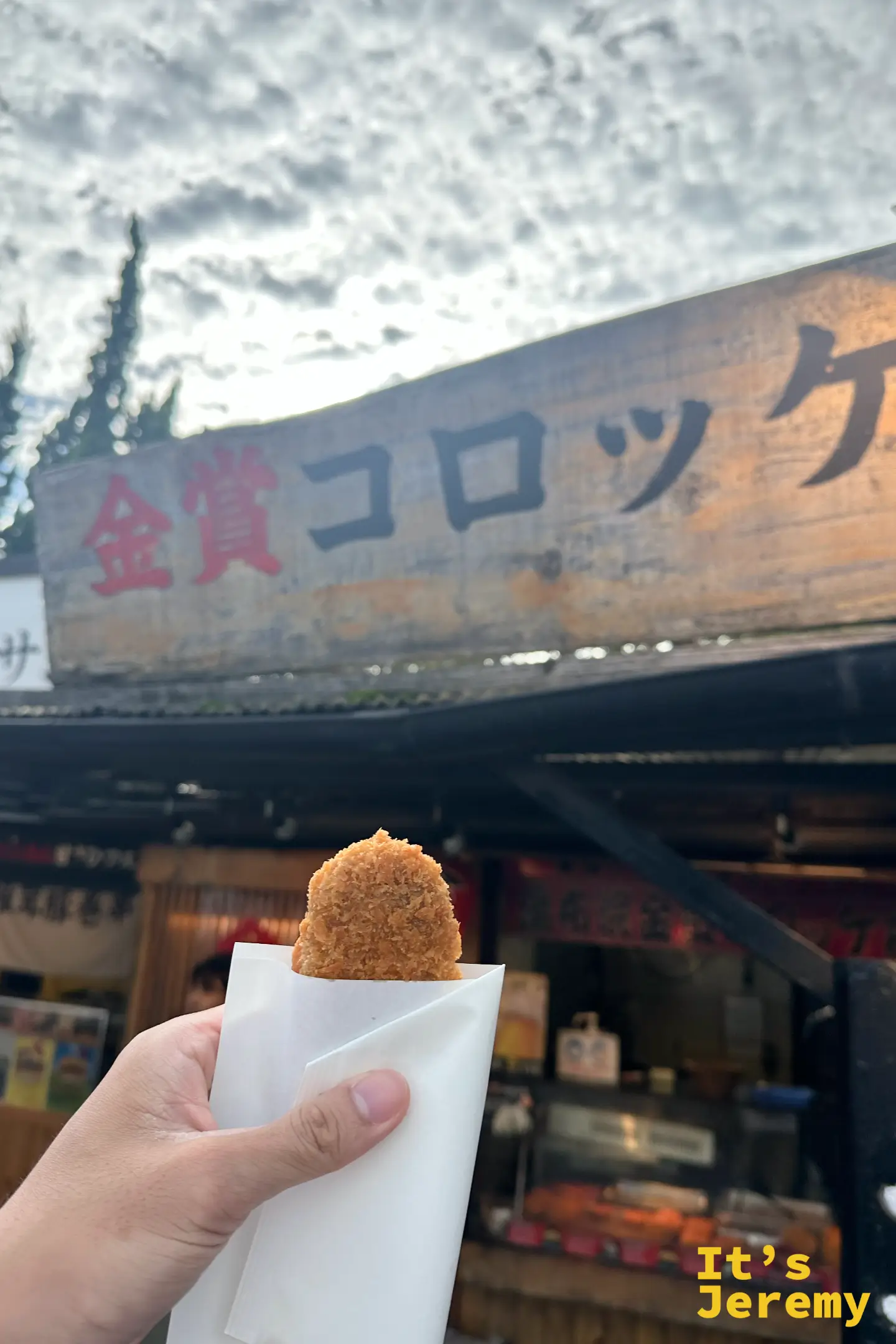 手拿一顆炸得金黃的金賞可樂餅，裝在白紙袋裡