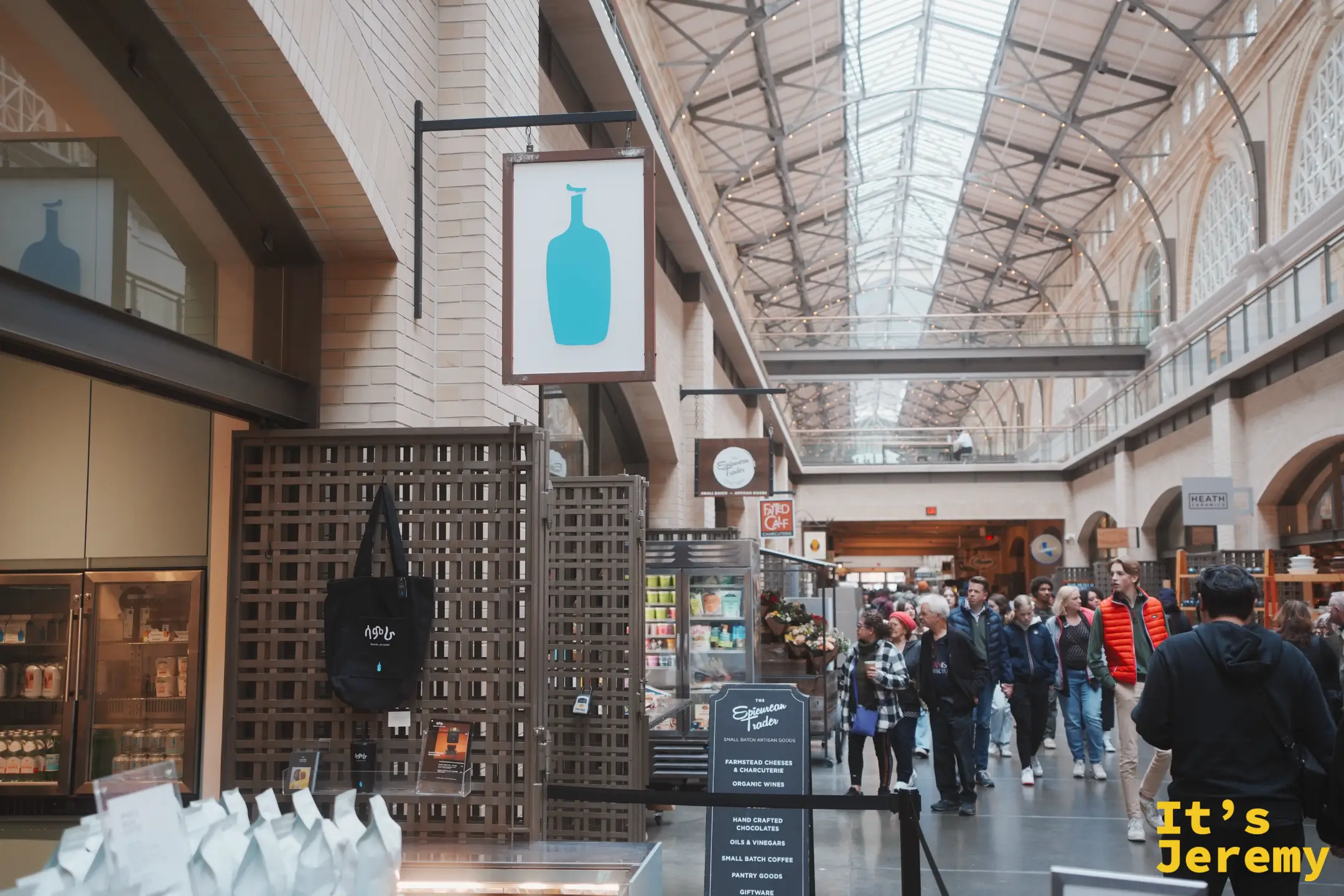 渡輪大廈內的 Blue Bottle 藍瓶咖啡招牌，旁邊是 The Epicurean Trader 精選食品店的立牌，人潮沿著長廊移動