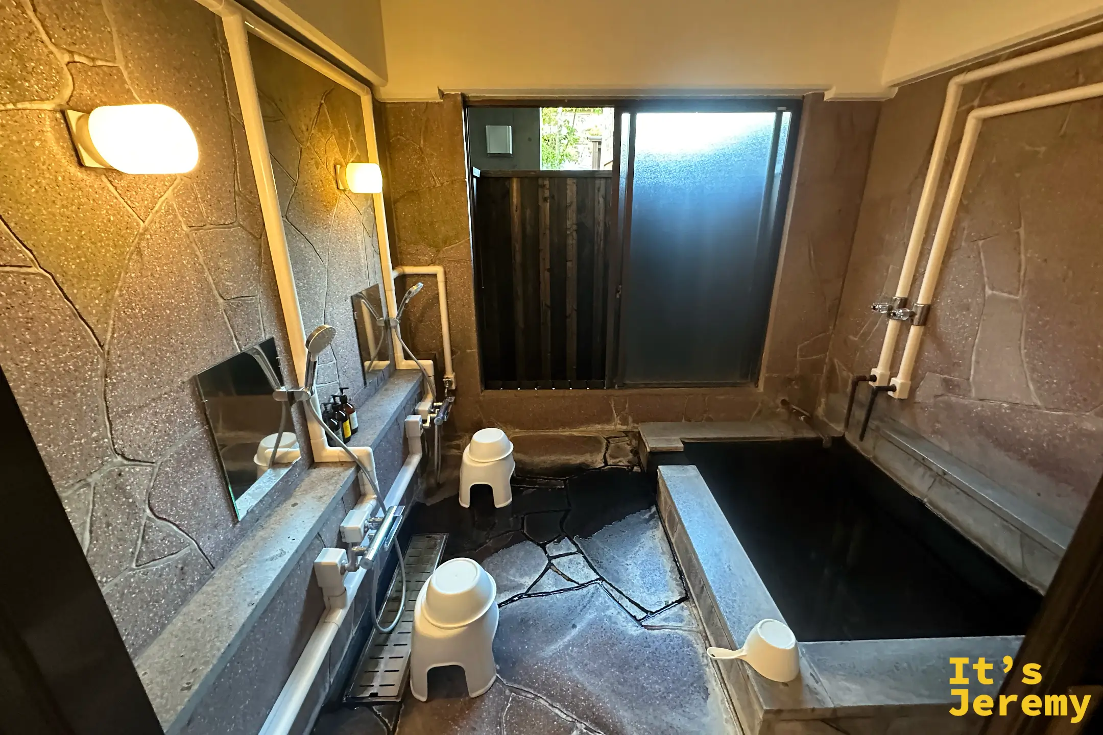 榎屋旅館一樓的貸切湯屋，石造浴池與洗澡區，牆面鋪石材，木柵欄採光窗