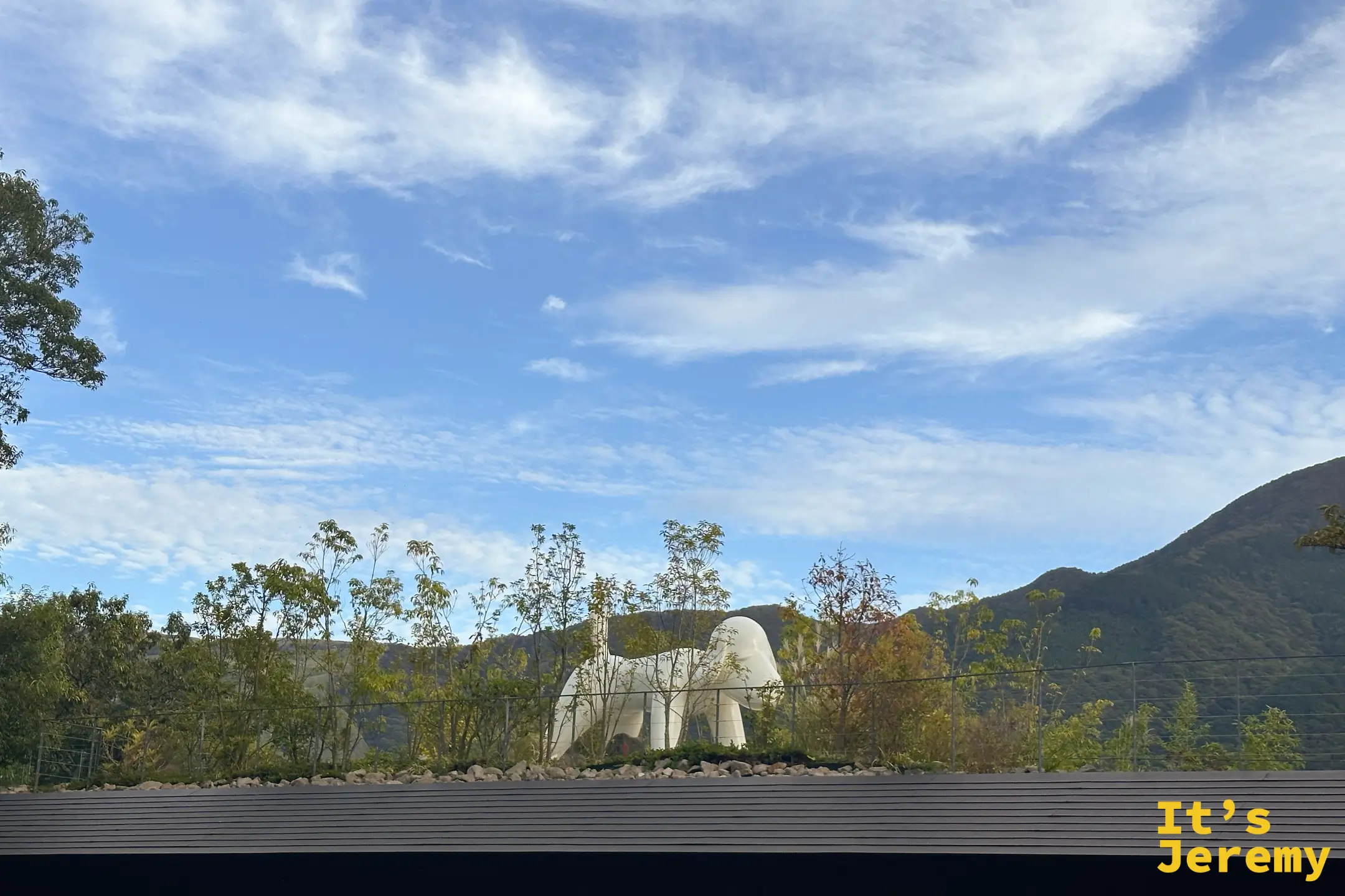 黑色建築屋頂上立著一座白色大狗雕塑，背後藍天遠山