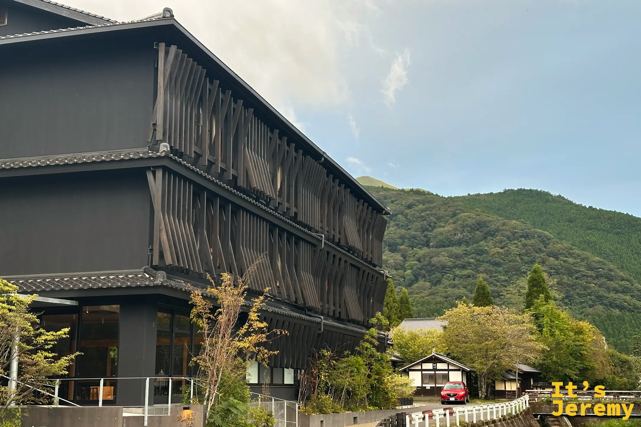 榎屋旅館的外觀，深色木造建築立面以斜向木格柵拼出紋理，背後是青山
