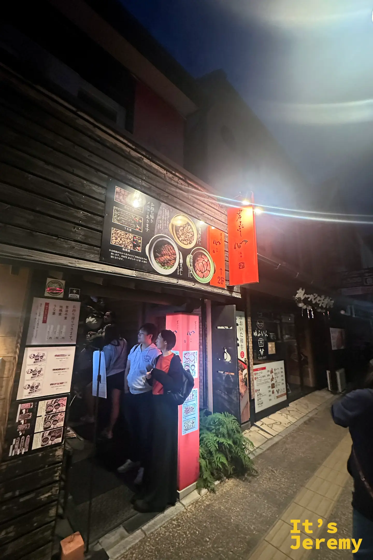 由布まぶし 心夜晚的店面外觀，木造牆面掛滿菜單海報，橙色招牌