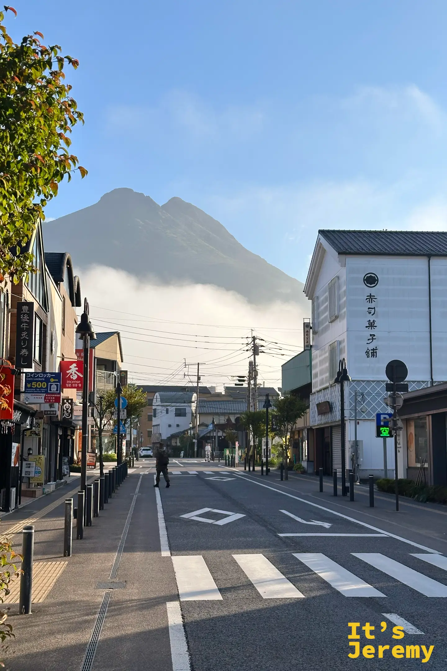 由布院湯之坪街道盡頭，由布岳立在老街後方，清晨山頭纏著一圈白雲