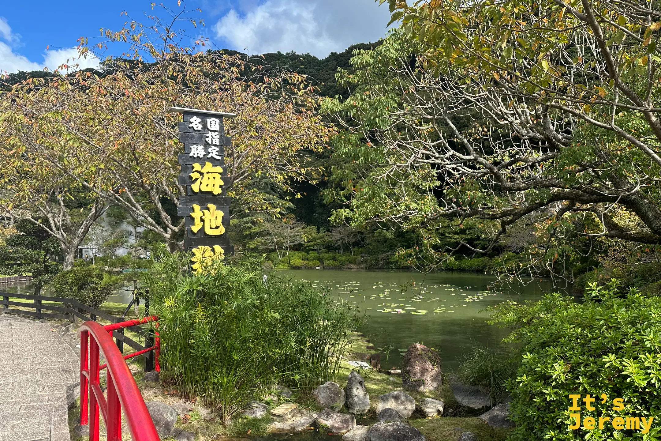入口庭園的蓮池，池畔立著黑底金字「国指定名勝 海地獄」石碑，前方有一座紅色小拱橋