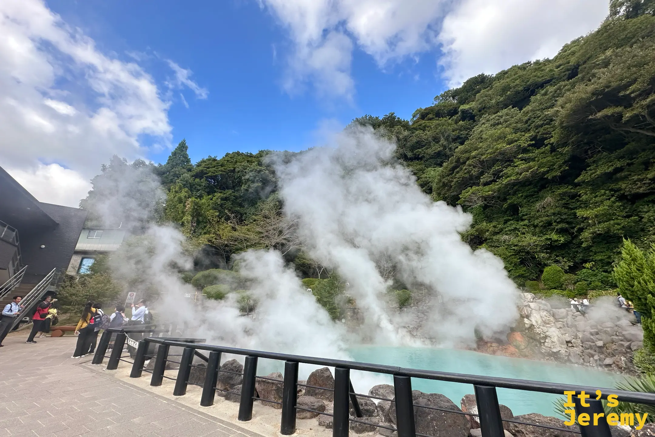 遊客沿著黑色欄杆觀看海地獄的藍池，背後是一整片綠色山坡