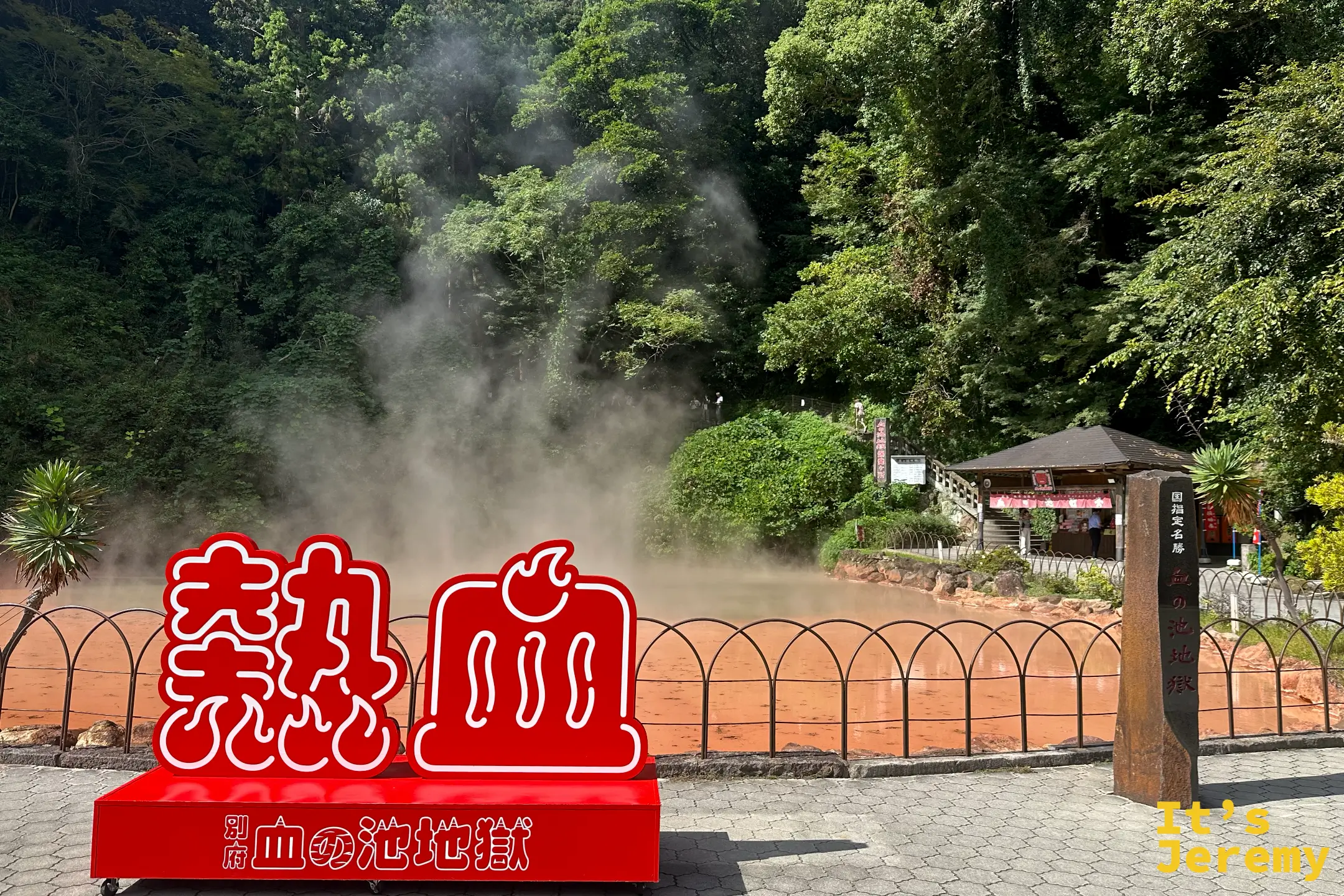 紅色的「熱」「血」立體打卡看板，寫著「別府 血の池地獄」，後方是紅褐色冒煙池與賣店