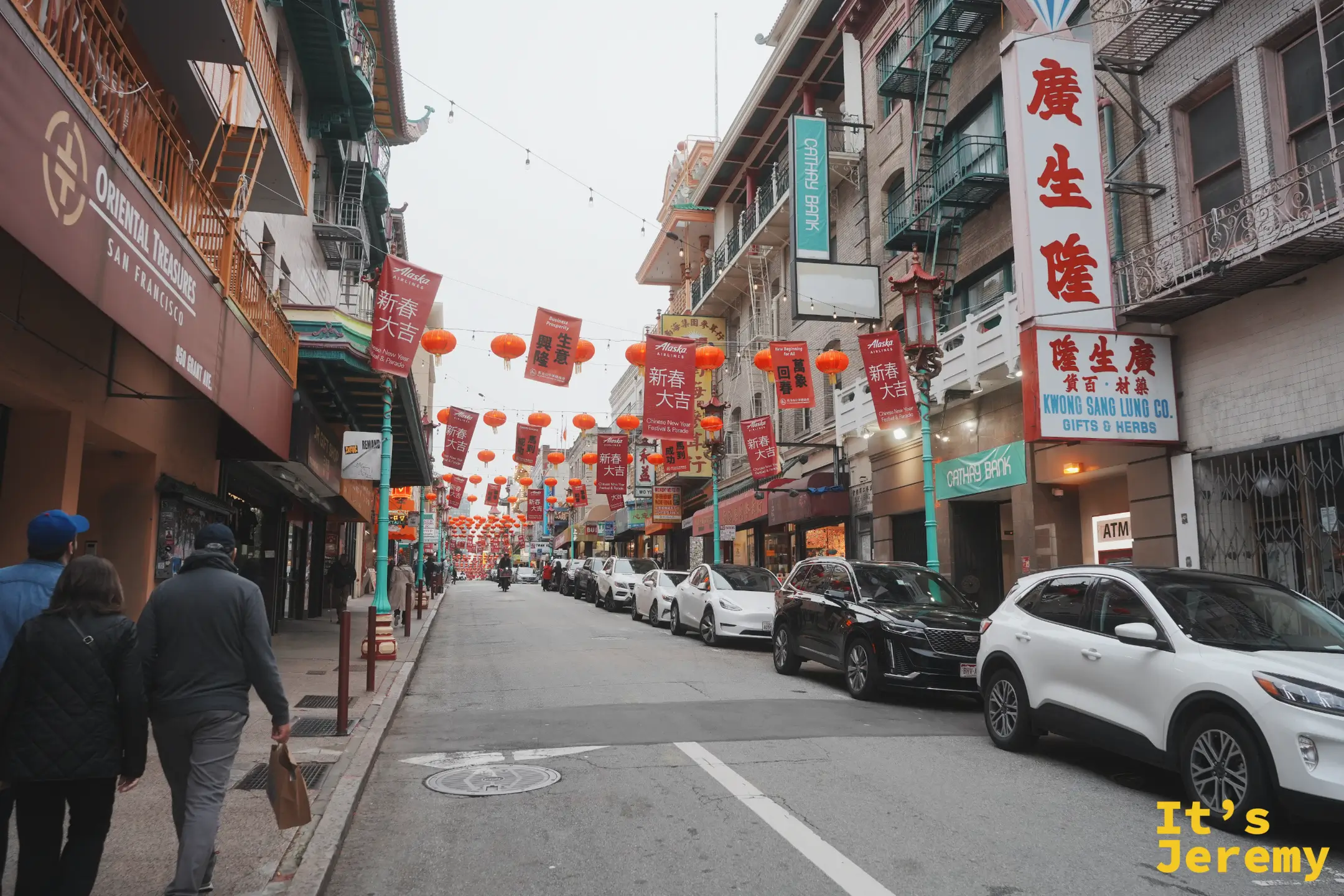 都板街街景，兩側商店招牌林立，頭頂掛滿紅燈籠與新春旗幟，遠方是綠色龍柱路燈與行人
