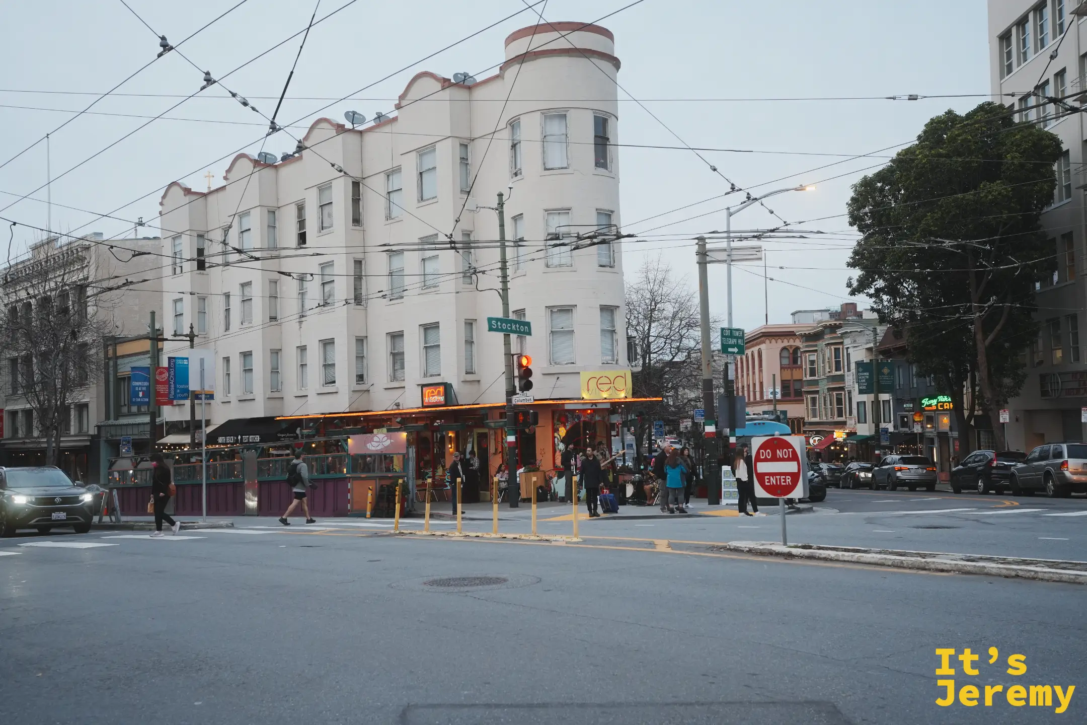 Columbus 與 Stockton 路口的白色圓角老樓，路牌指向科伊特塔與電報山，天色轉暗