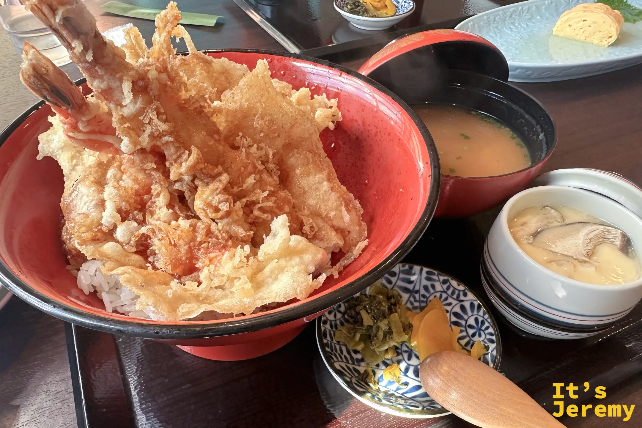 とよ常的特盛天丼，三尾巨大的炸蝦直挺挺插在紅色丼碗的白飯上，旁邊配著味噌湯、茶碗蒸與漬物