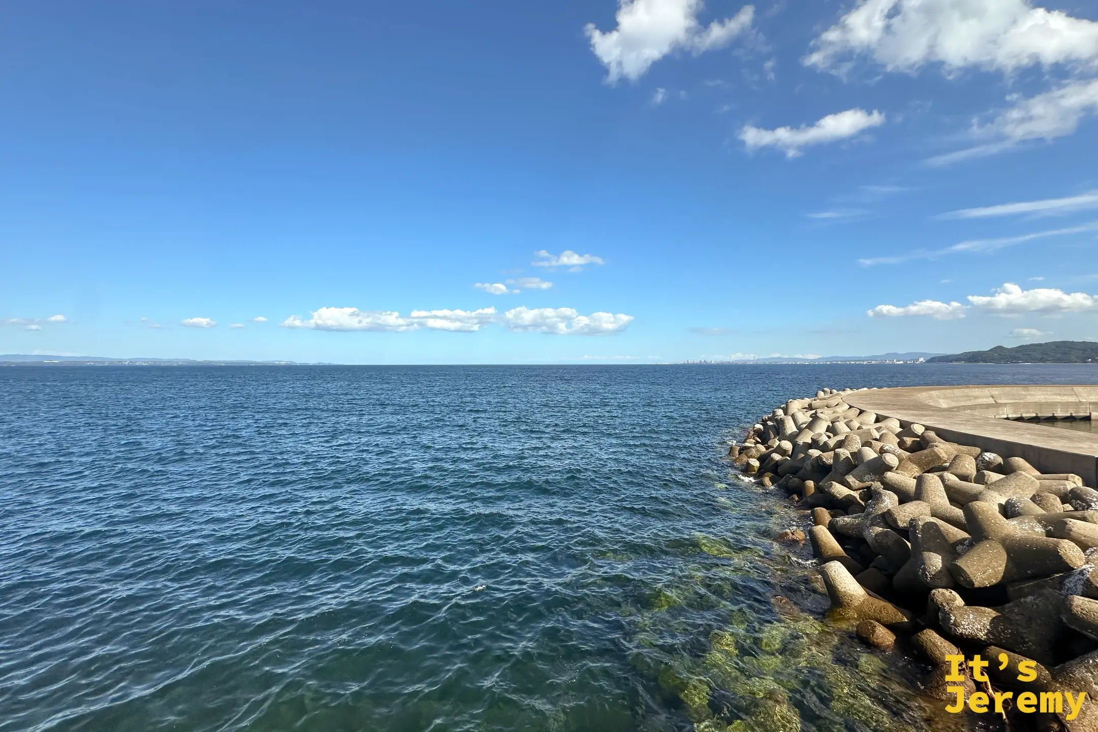 別府灣的海堤邊，消波塊一路排進海裡，海面湛藍、遠方天際線有雲