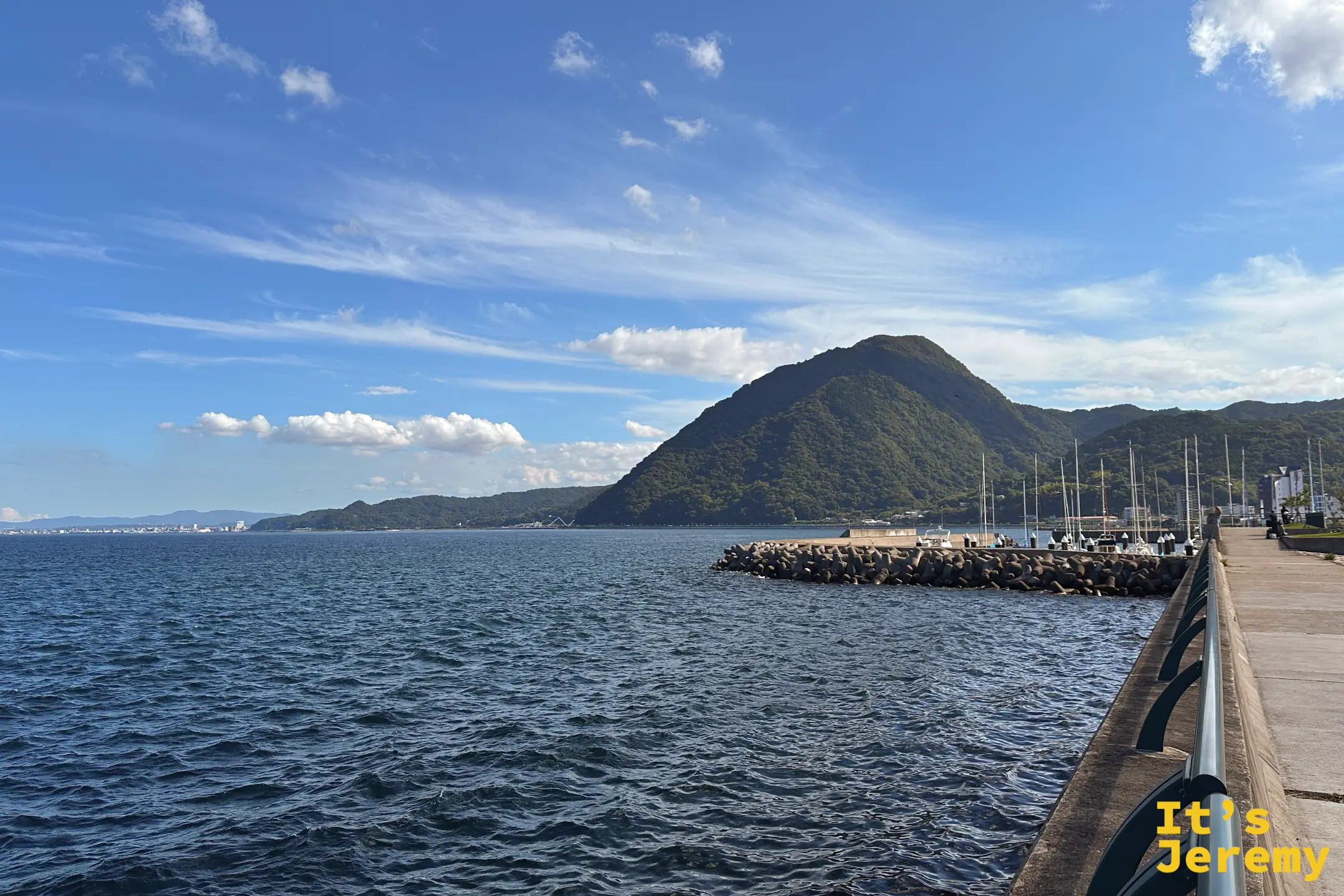 防波堤一路延伸進別府灣，盡頭正對著那座圓錐狀的綠色小山與小漁港