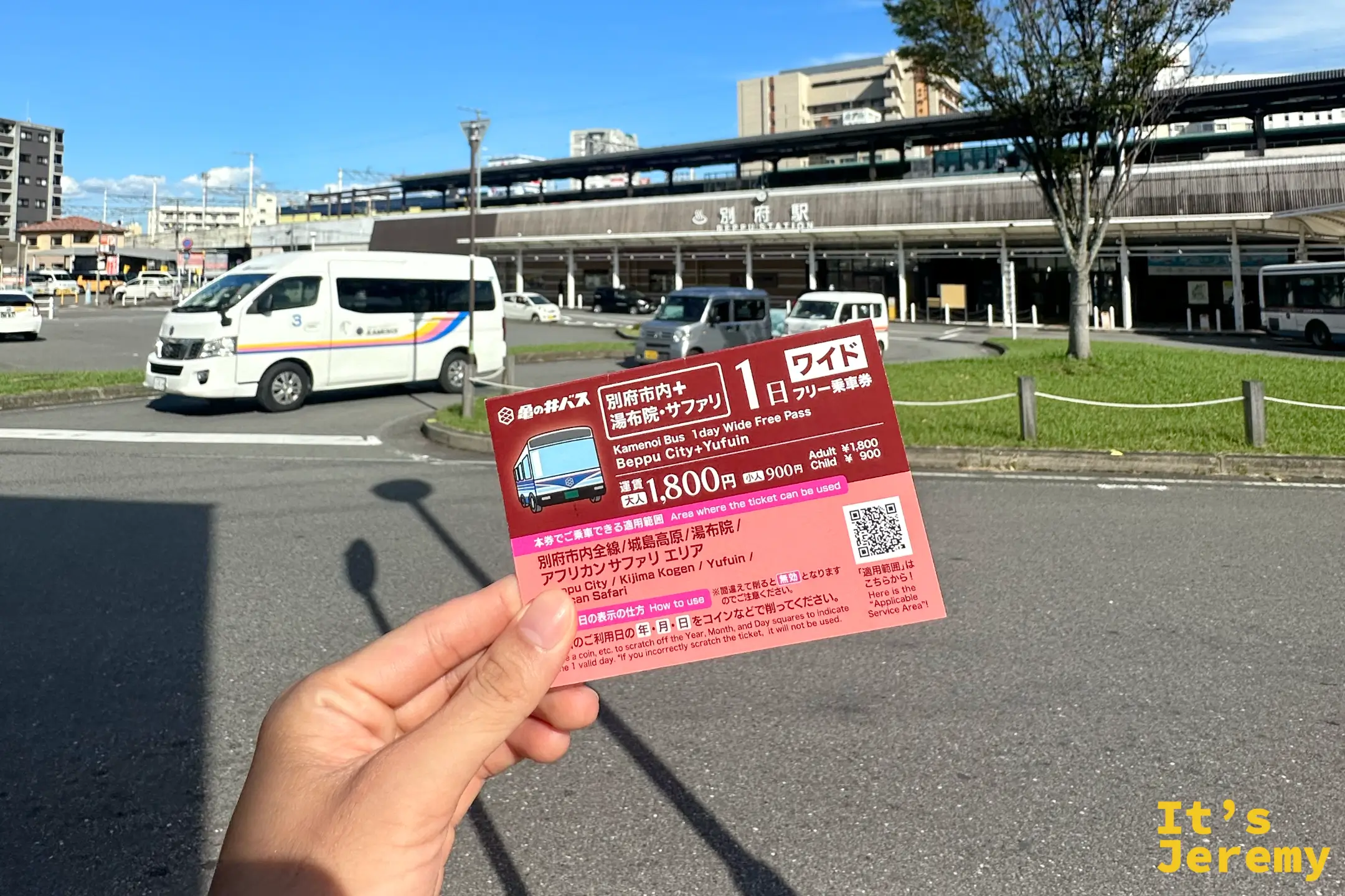 手裡拿著一張粉紅色的別府市內巴士一日乘車券，標示 1,800 日圓、由布院・別府通用