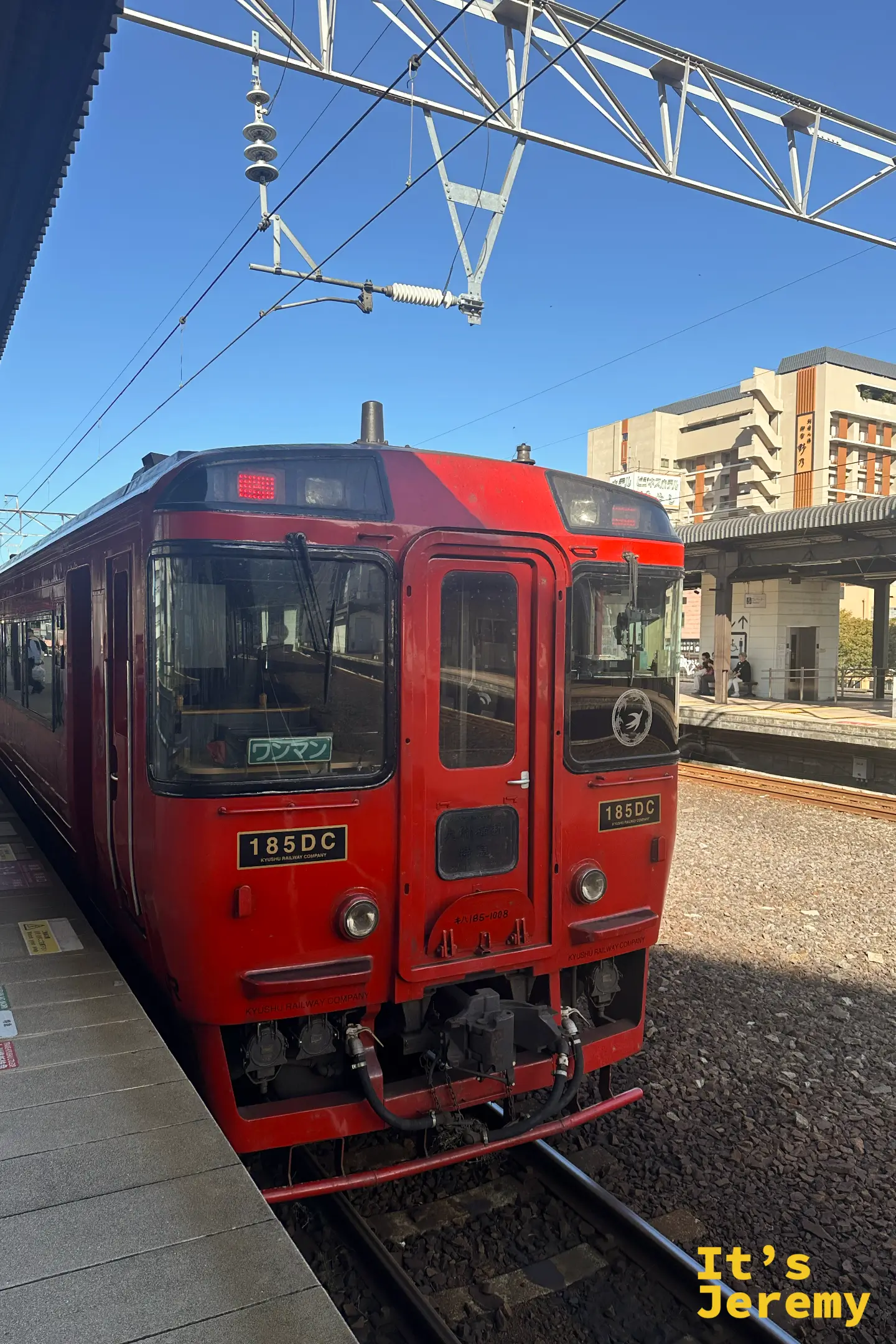 別府車站月台上一列鮮紅的九州横断特急列車，車身印著 185DC