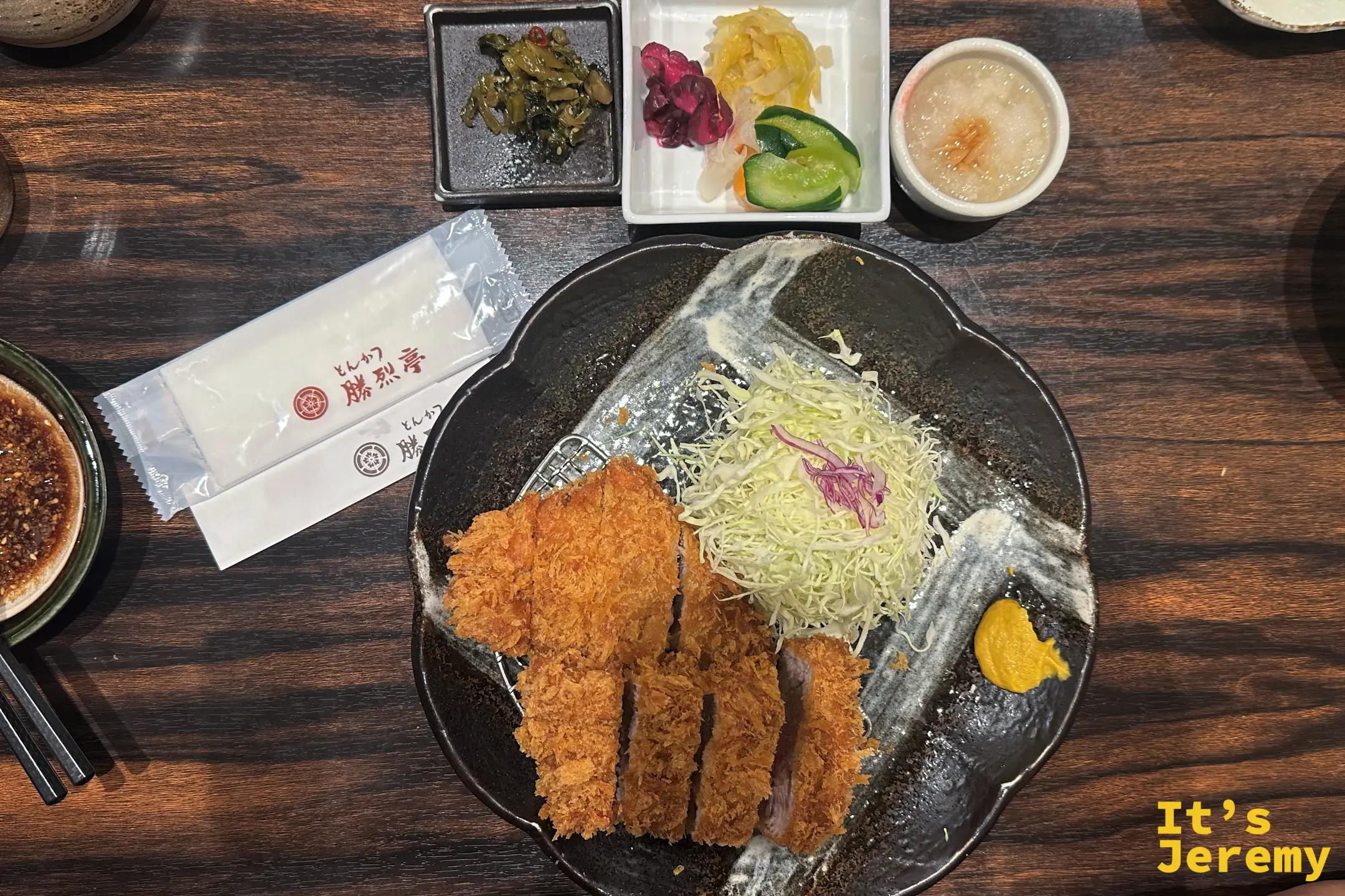 勝烈亭的招牌厚切炸豬排，炸衣蓬得像雪花，一旁附高麗菜絲、黃芥末與現磨芝麻醬碗