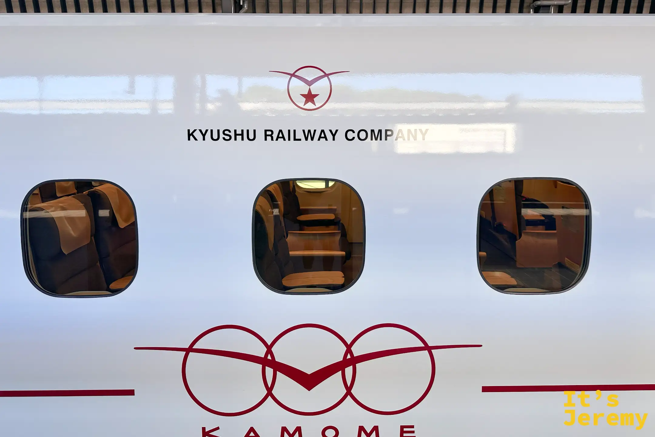 隔著車窗看かもめ車廂內的暖橘色皮椅與木質桌板，Kyushu Railway Company 標誌