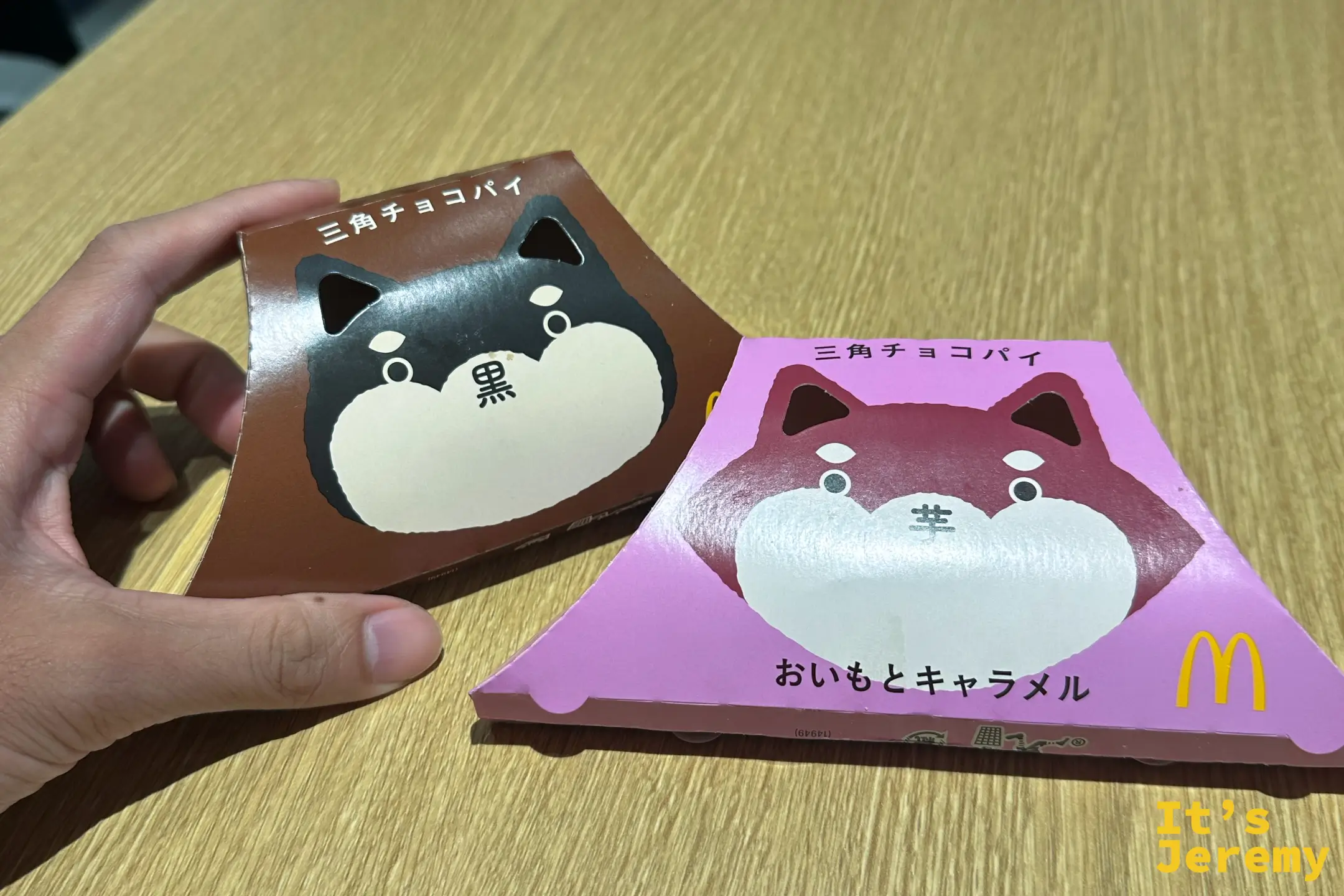 手拿兩個麥當勞三角チョコパイ，黑巧克力口味的黑柴犬包裝與地瓜焦糖口味的紅柴犬包裝