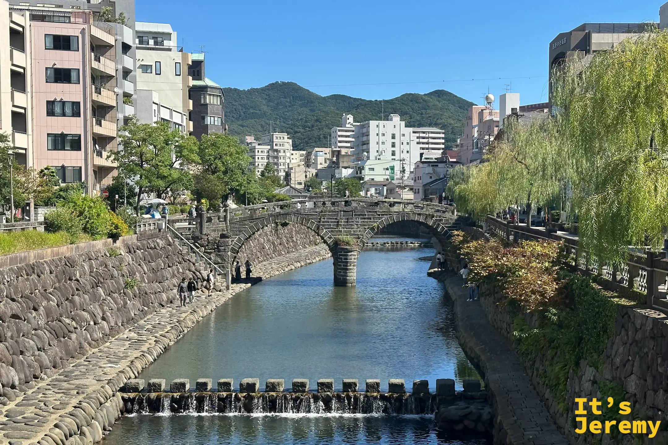 稍遠處俯看眼鏡橋橫跨中島川，橋與兩岸市街構成一幅安靜的長崎日常