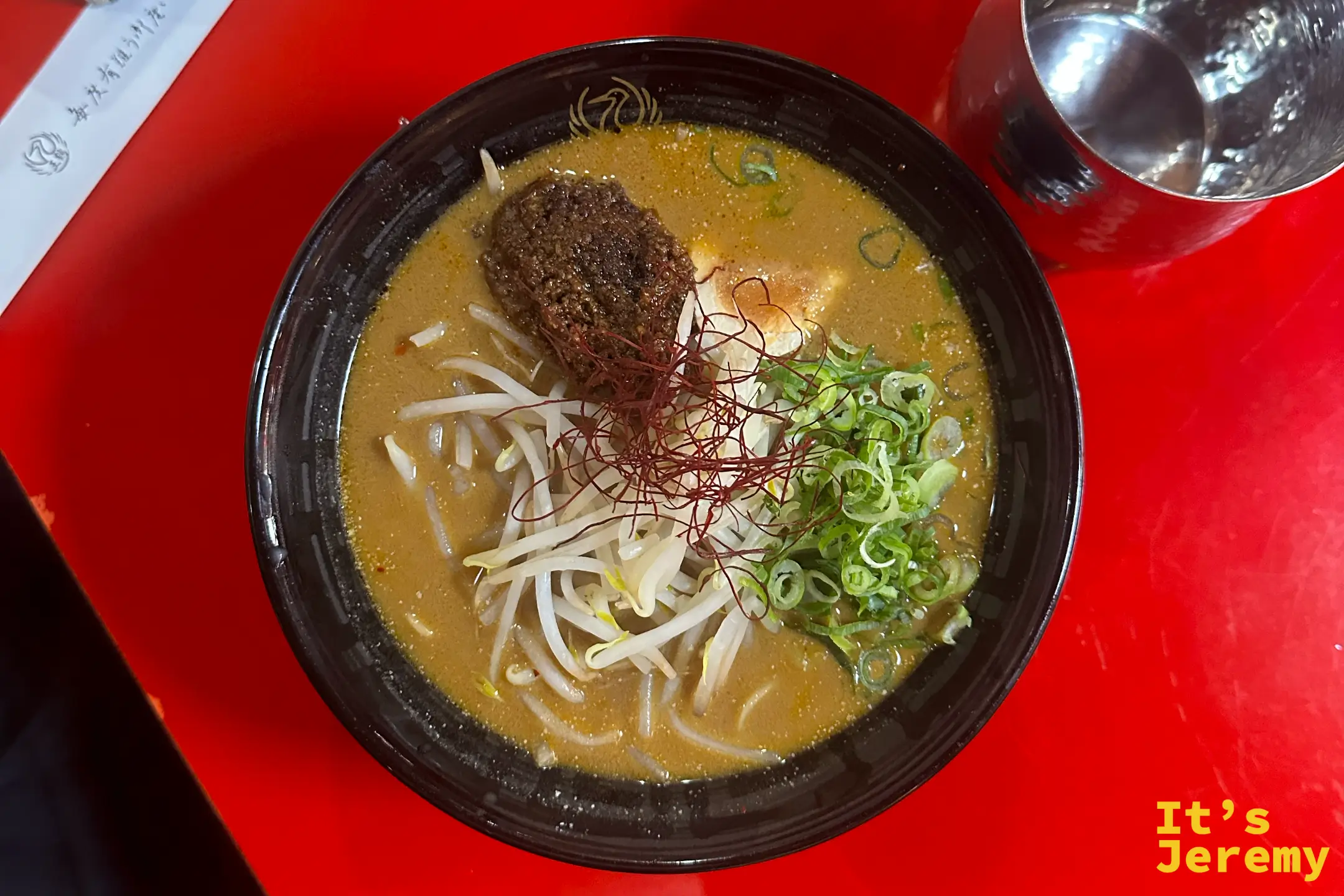深褐色湯頭的擔擔麵，鋪著肉味噌、豆芽、紅色辣椒絲與蔥花