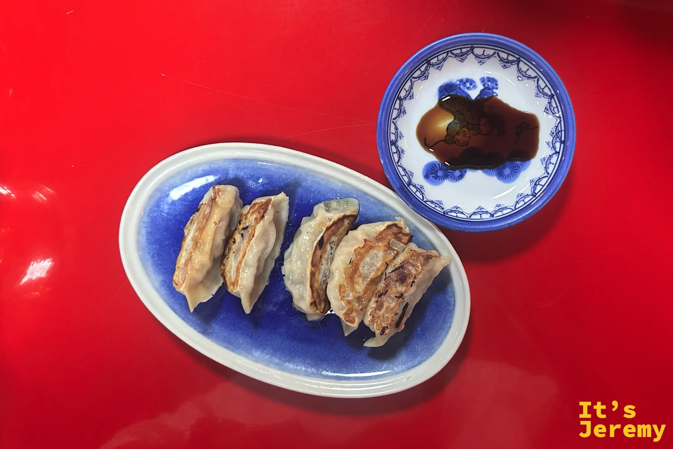 藍色橢圓盤上的五顆煎餃，旁邊附沾醬