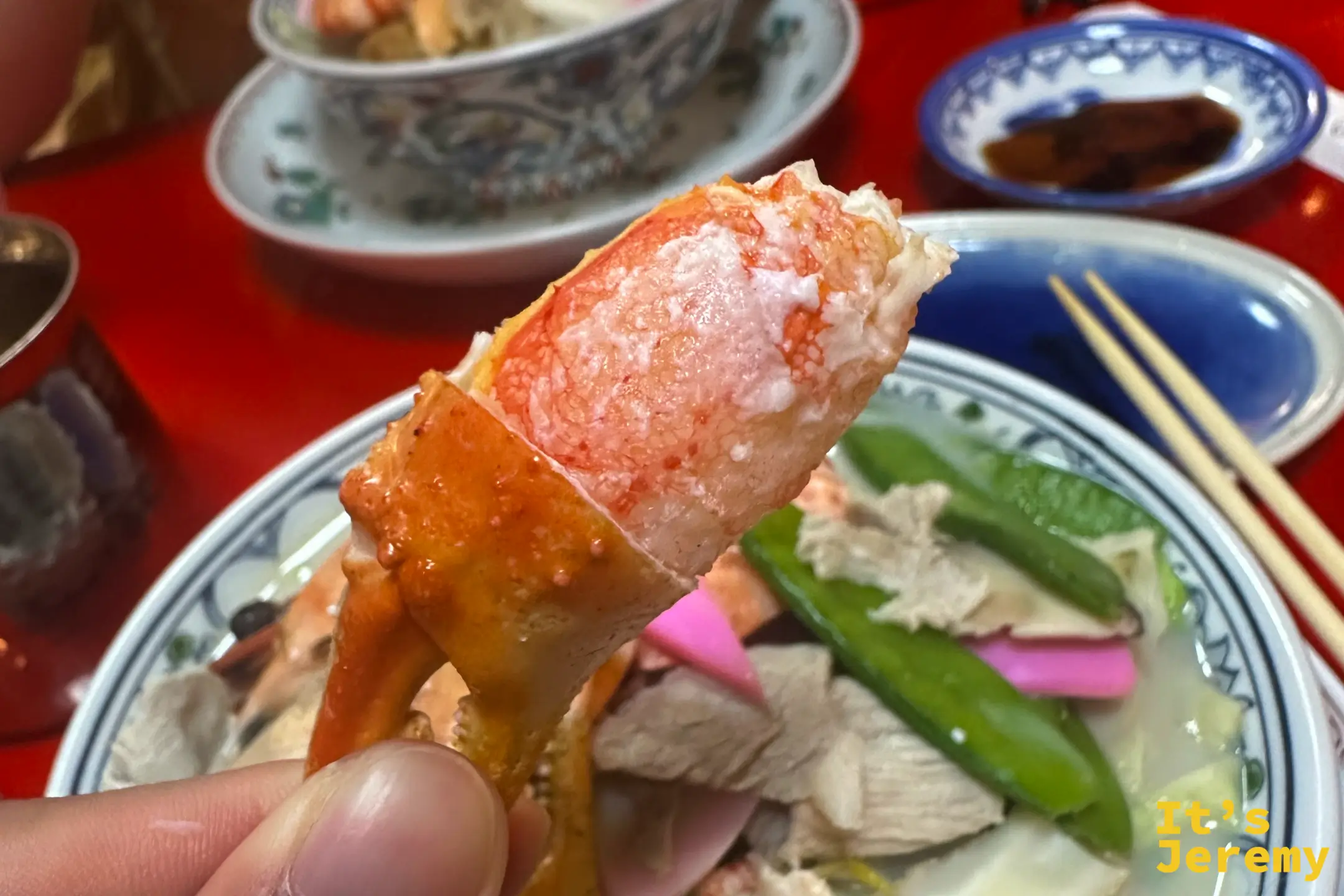 手拿一隻蟹螯，背後是滿滿海鮮的強棒麵大碗