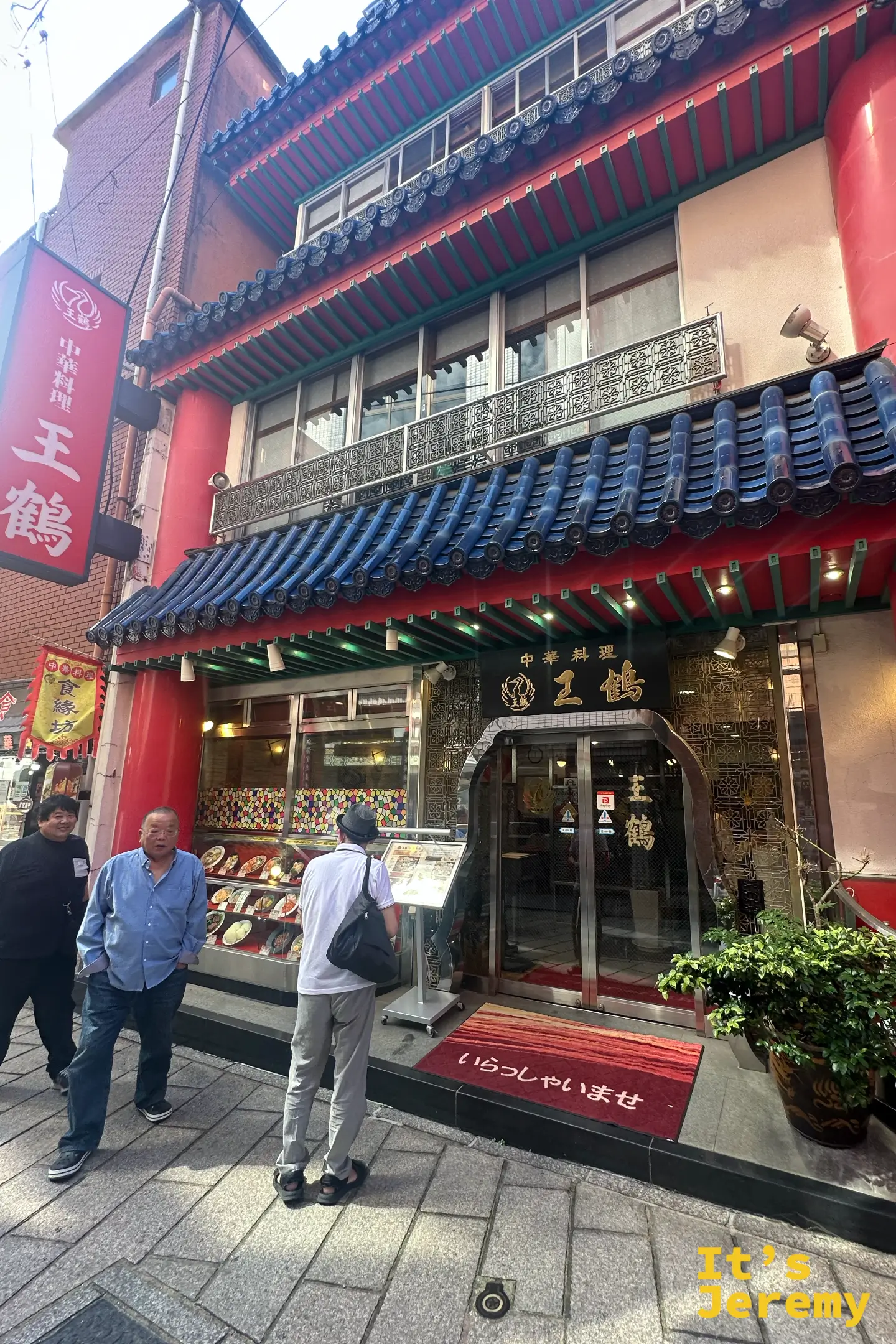 王鶴店面外觀，紅色建築搭配藍色屋瓦，門口有人在看菜單