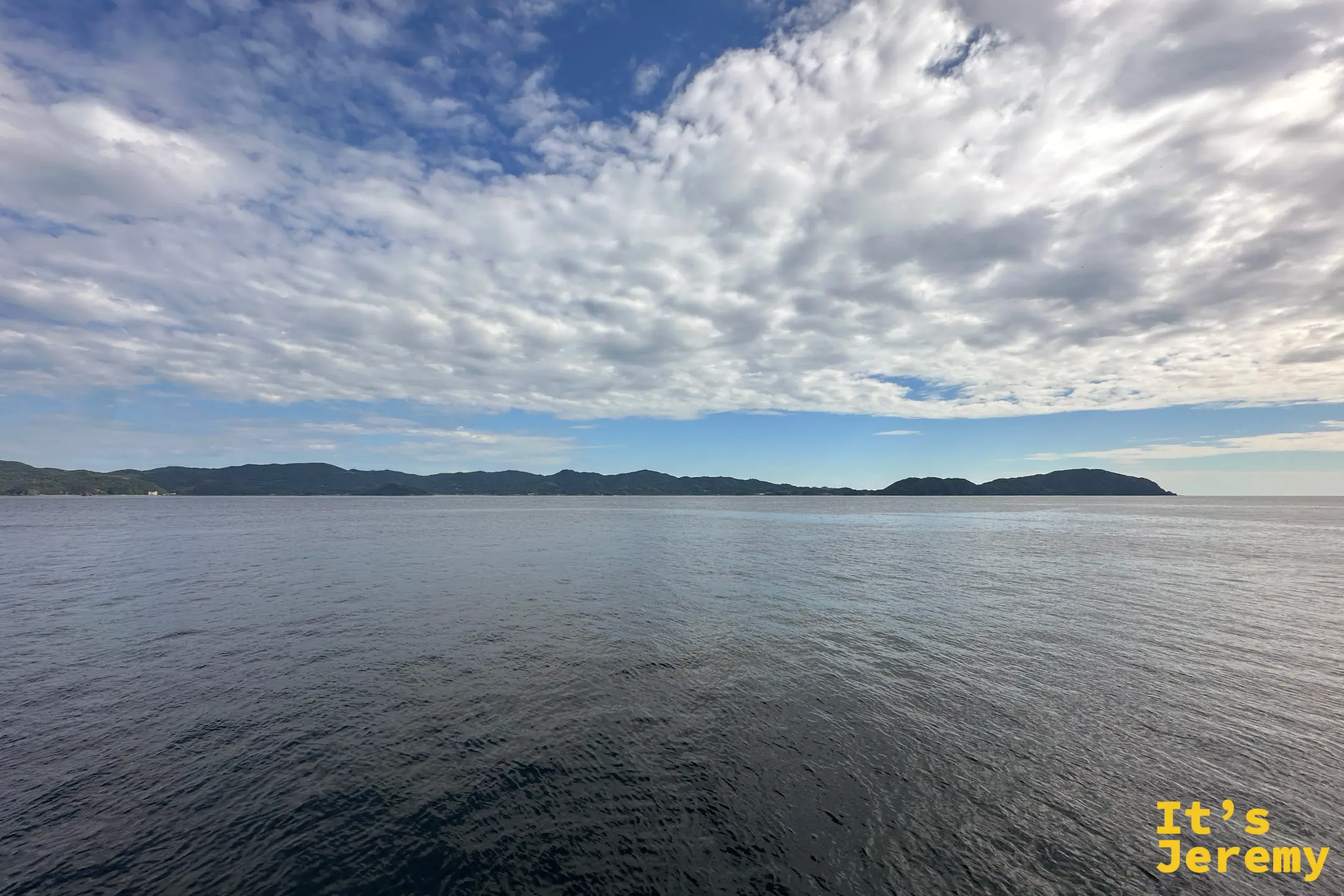 開闊的海面與遠處連綿的海岸線、雲影