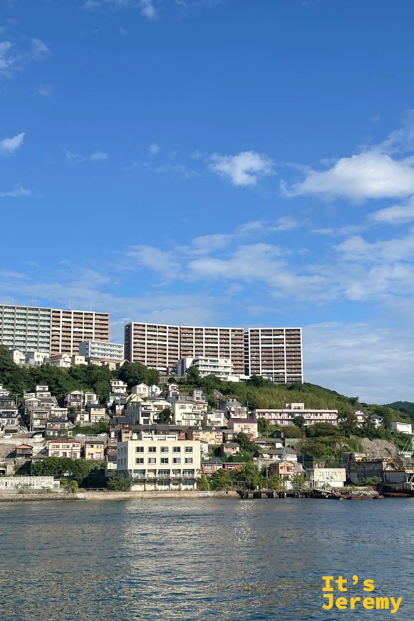 長崎港灣邊層層疊疊的山坡住宅，山頂並排著幾棟大型集合住宅