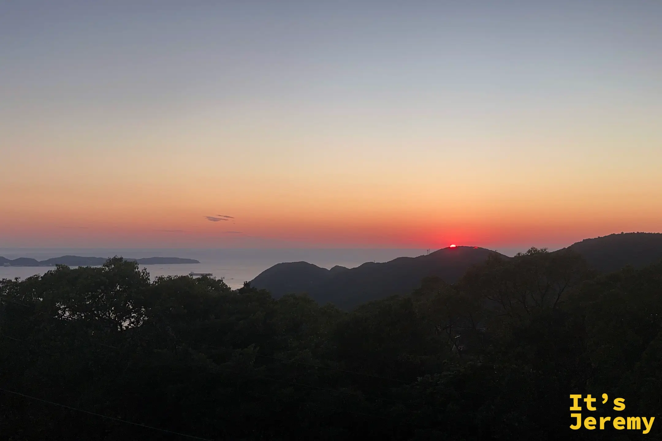 稲佐山望向海面的黃昏，夕陽化成一顆紅點沉落在遠方山稜線上，海面與島嶼成剪影