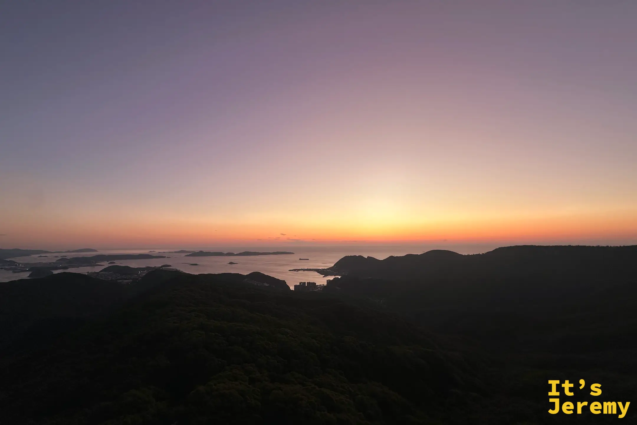 黃昏時分紫橘漸層的天空，山巒與海灣層層退向遠方