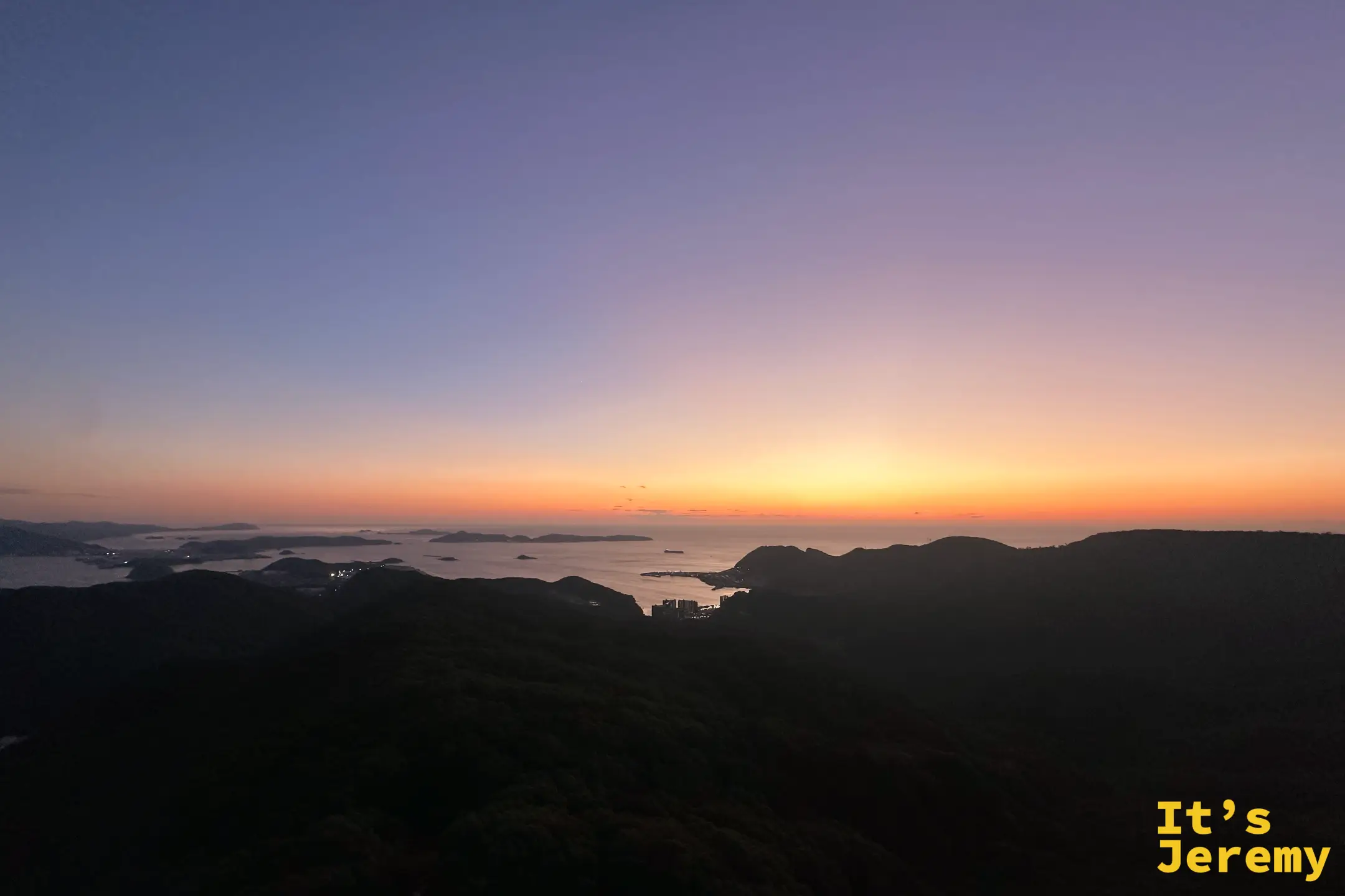 夕陽沉入海平面，天空橘紅、前景是深色的山稜線