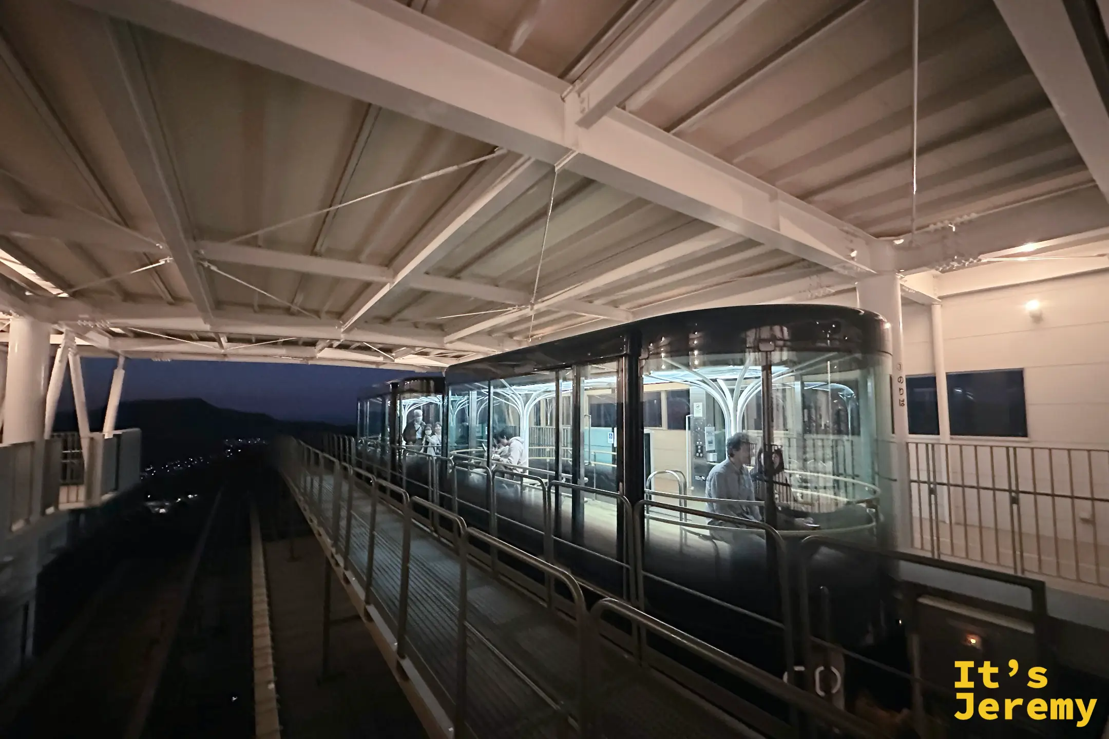 稲佐山山頂站月台上的玻璃車廂斜坡電車，車內有乘客，月台旁的軌道沿陡坡往山下延伸