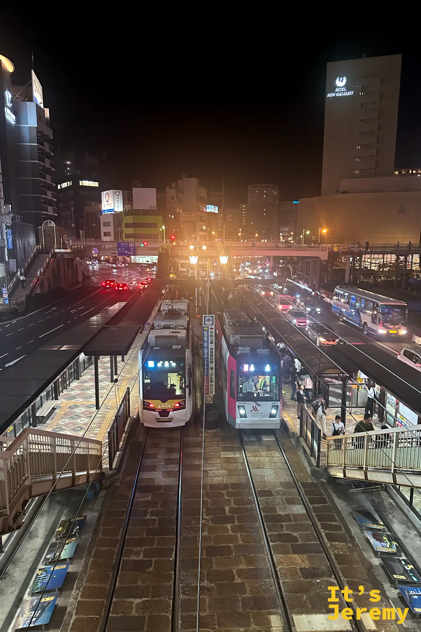 夜裡從天橋俯看長崎的路面電車站，兩列電車停靠在石砌軌道邊，遠處是 HOTEL NEW NAGASAKI 的燈
