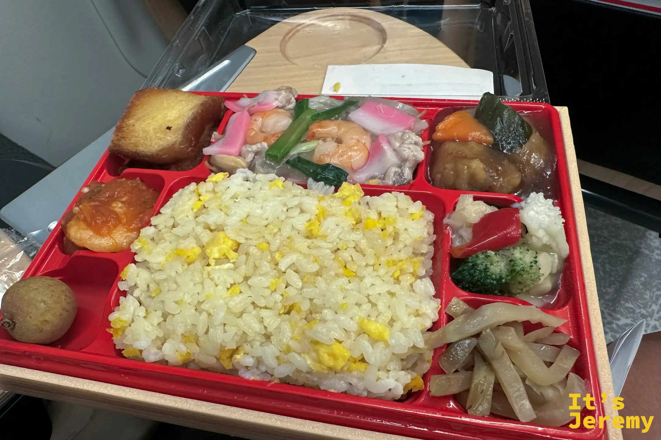 車上打開一盒紅色分隔的中華炒飯便當，有蛋炒飯、蝦仁、什錦海鮮、花椰菜與醃菜