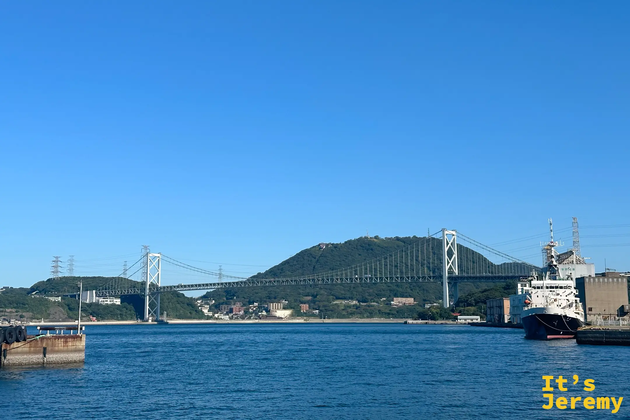 從門司港車站往海港方向遠眺平靜的關門海峽,壯麗的關門大橋橫跨海面,展現北九州門司港懷舊地區古今交織的靜謐海岸美景