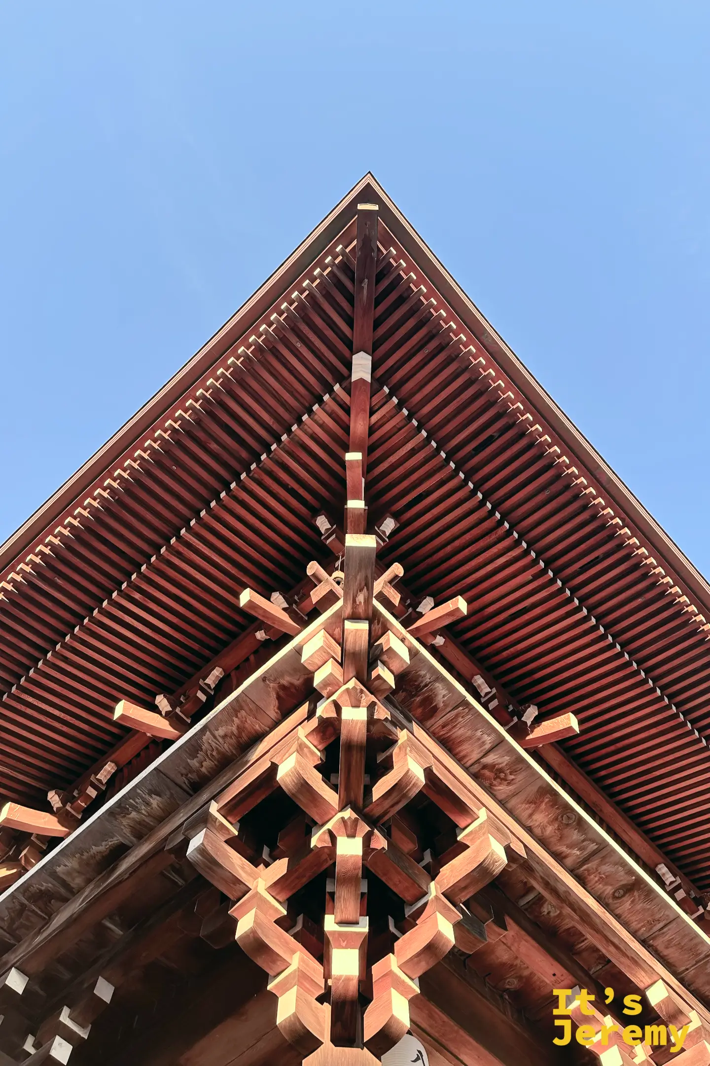 從小倉八阪神社東楼門正下方仰拍屋簷細節，繁複的木造斗拱在天空中形成完美的三角形構圖，展現日本神社建築美學