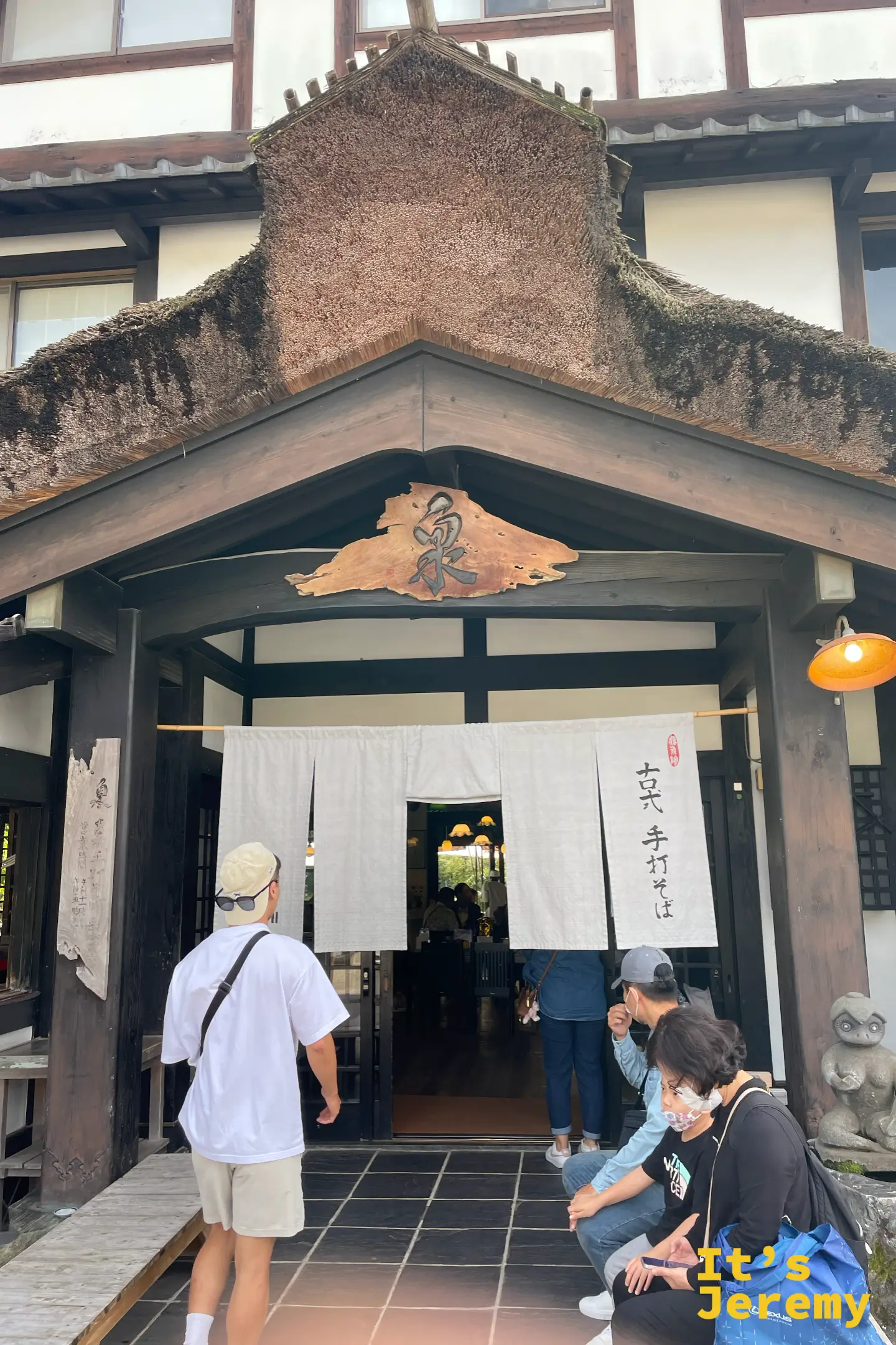 泉的入口門廊特寫，木造招牌寫著泉字，白暖簾寫古式手打そば，客人正要入店