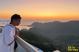 夕陽下的稲佐山山頂，一名遊客倚著欄杆望向橘紅色的海與山