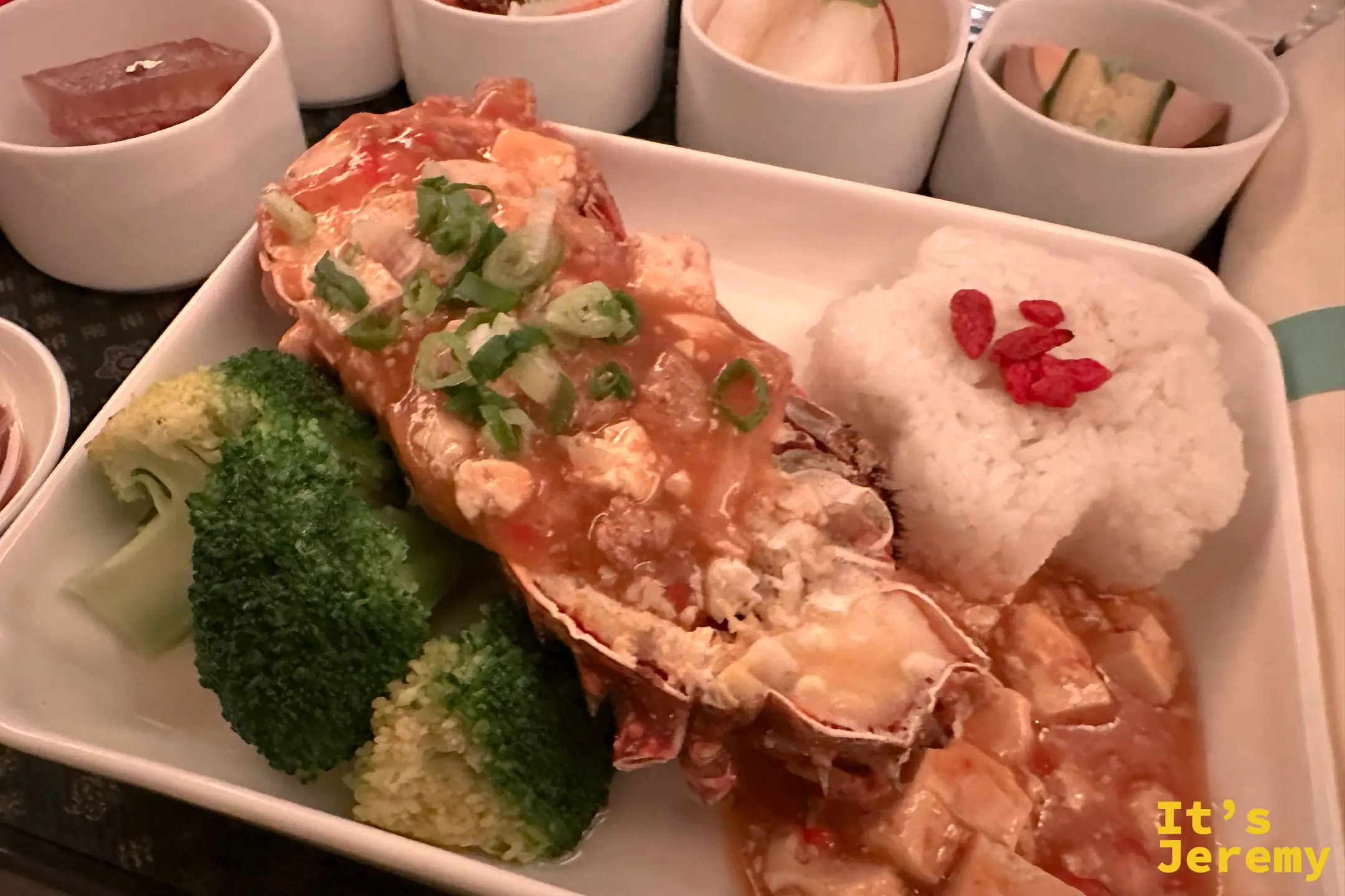 中華航空商務艙的龍蝦特寫，蝦肉上鋪滿豆腐辣醬與蔥花，配燙青花菜與花形白飯